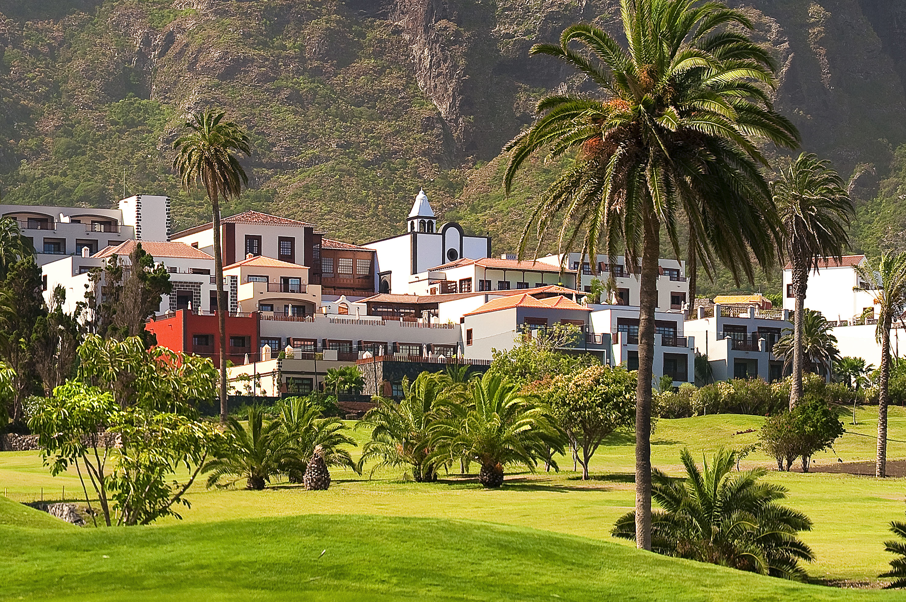 Mountain resort with palm trees, white buildings, and a lush green golf course.