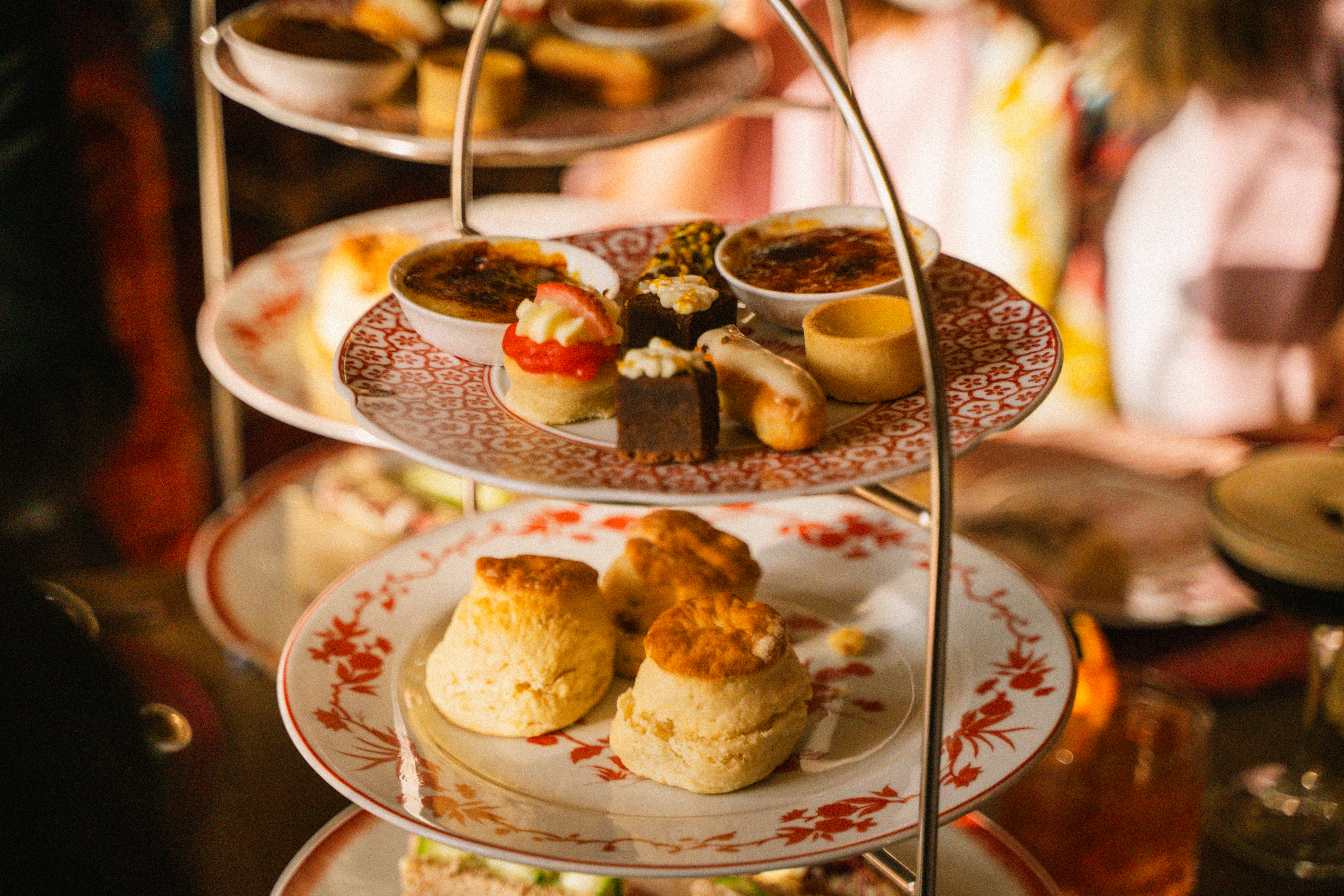 Afternoon tea tiered stand with scones, assorted pastries, and crème brûlée.