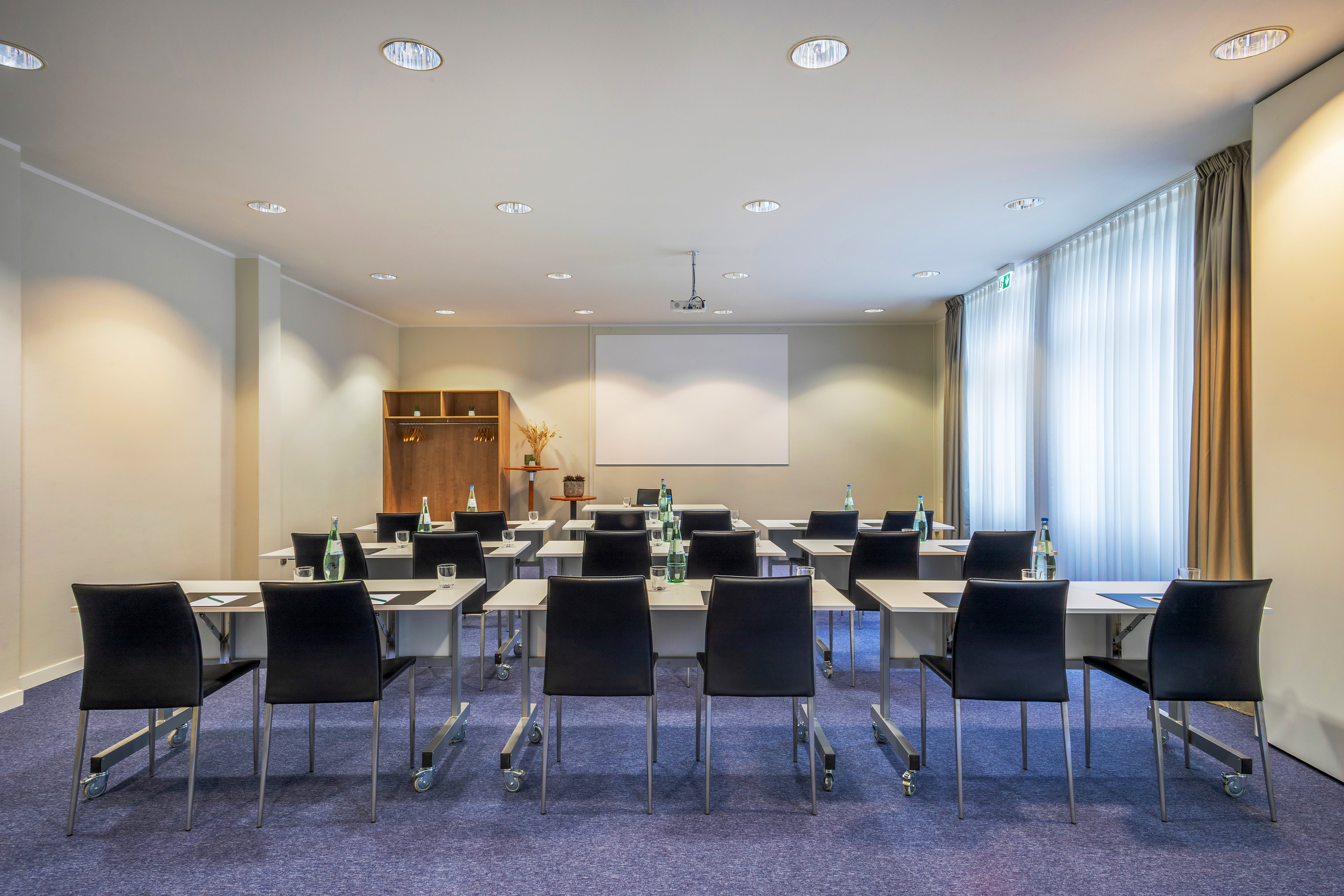 Modern meeting room with classroom setup, projector screen, and tables.