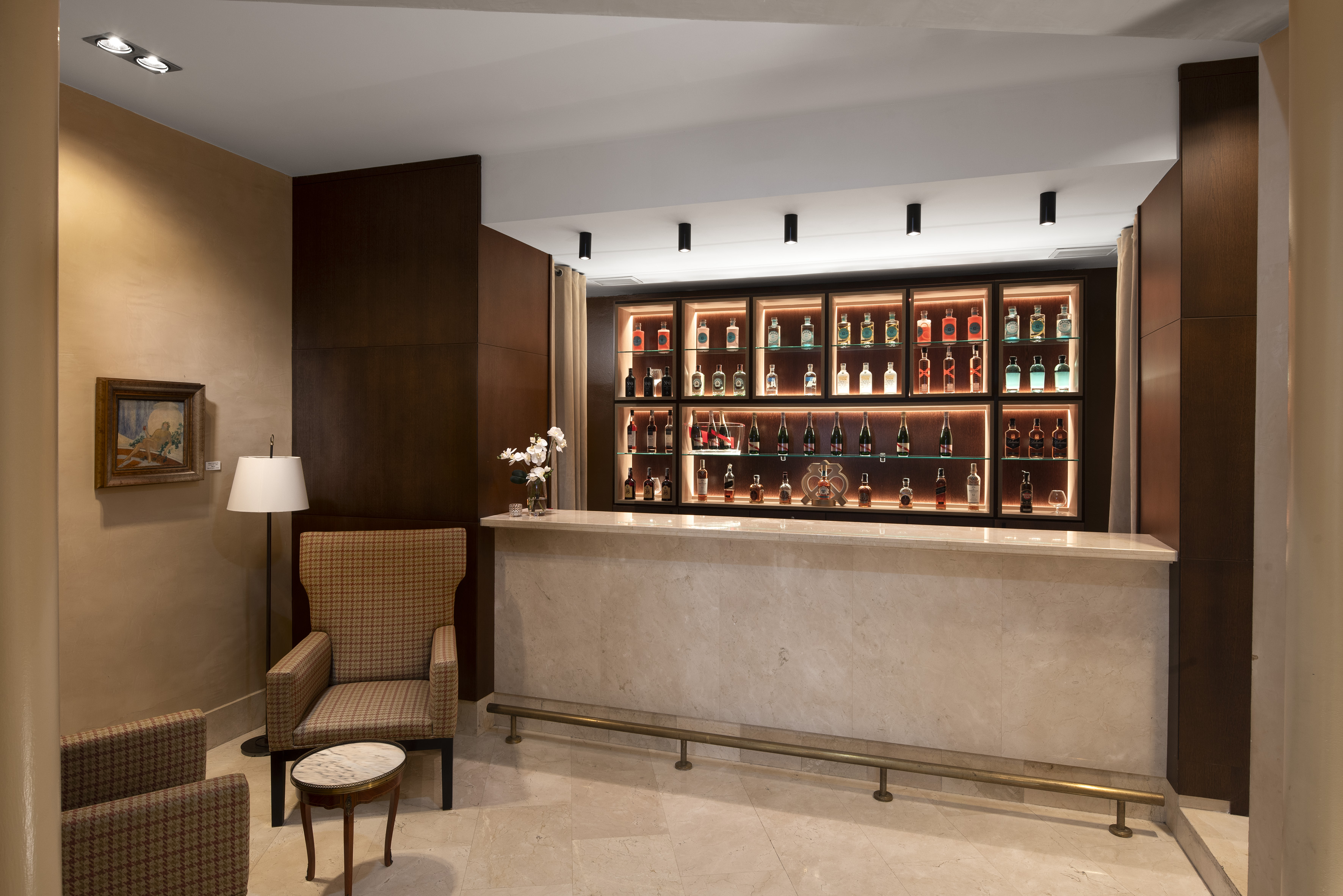 Modern bar with backlit liquor display, marble counter, and lounge chairs.