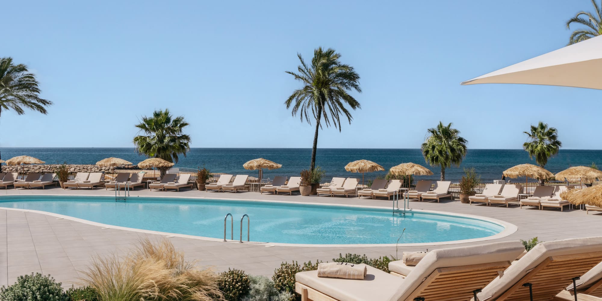 a pool with lounge chairs and umbrellas by the ocean