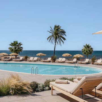 a pool with lounge chairs and umbrellas by the ocean