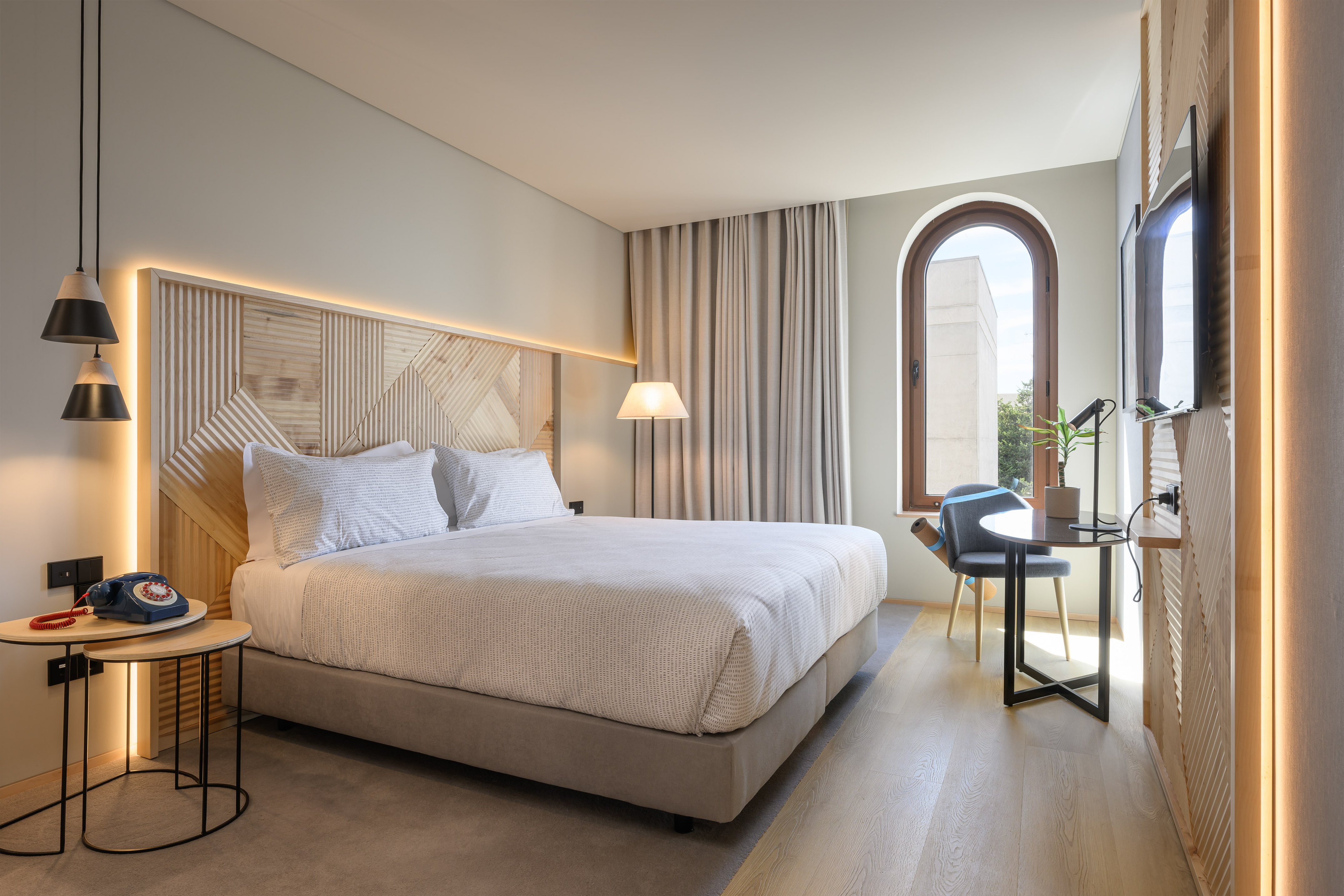 Modern hotel bedroom, wooden headboard, arch window, and contemporary decor.