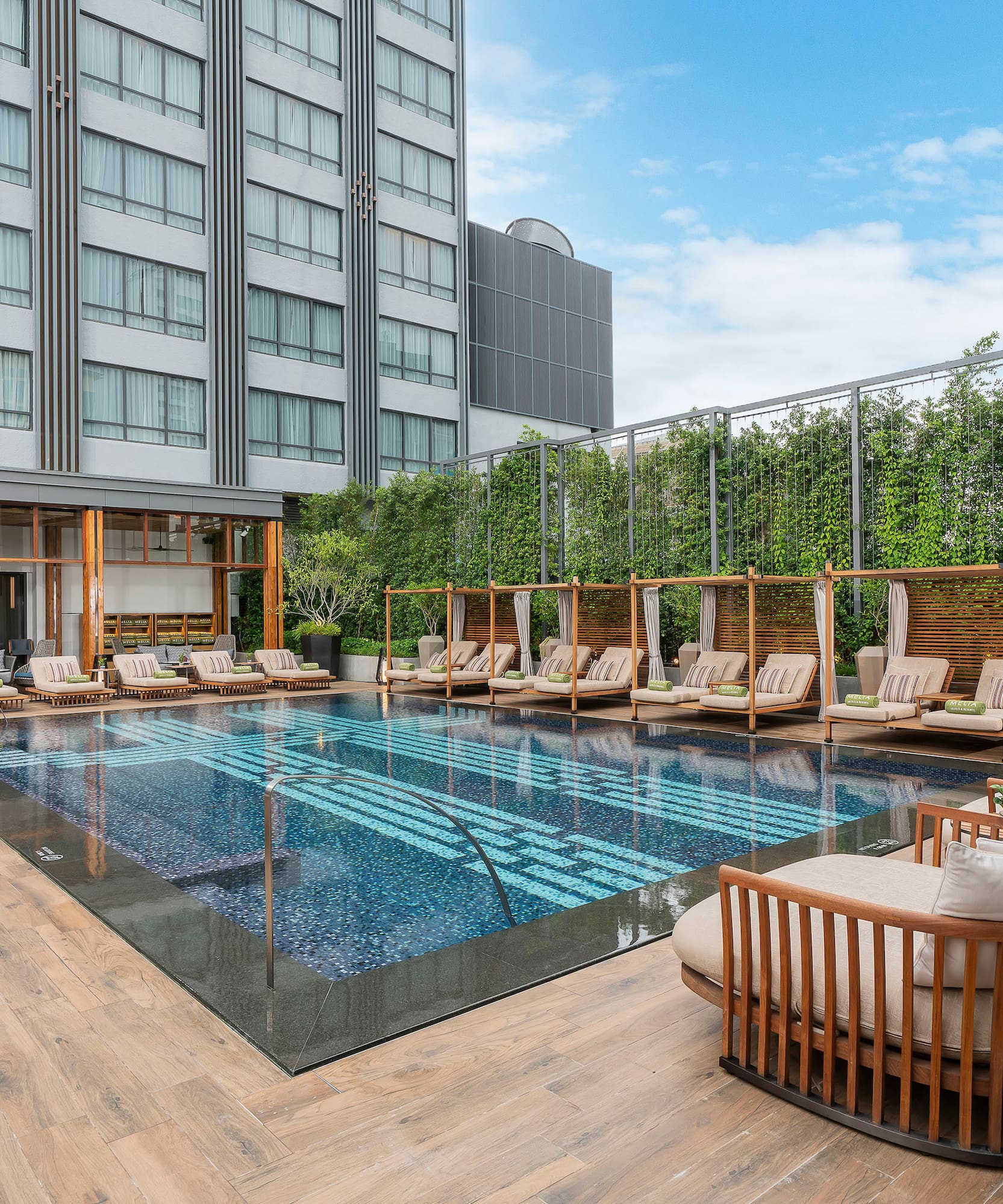 Piscina de hotel moderna con tumbonas, cabañas y vegetación frondosa.