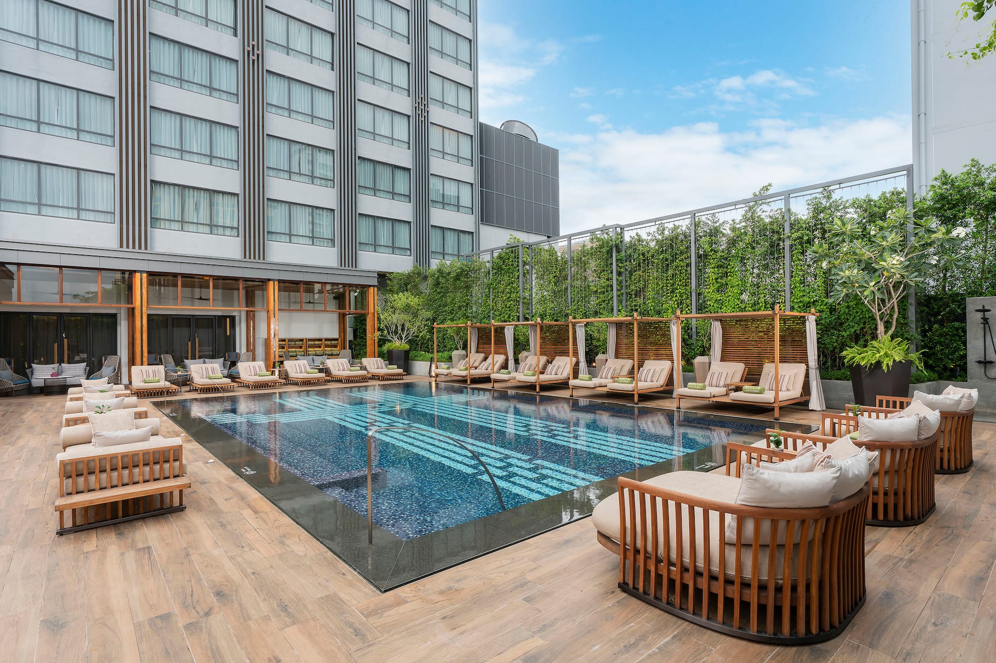 Luxury hotel pool area with sunbeds, cabanas, and modern building.