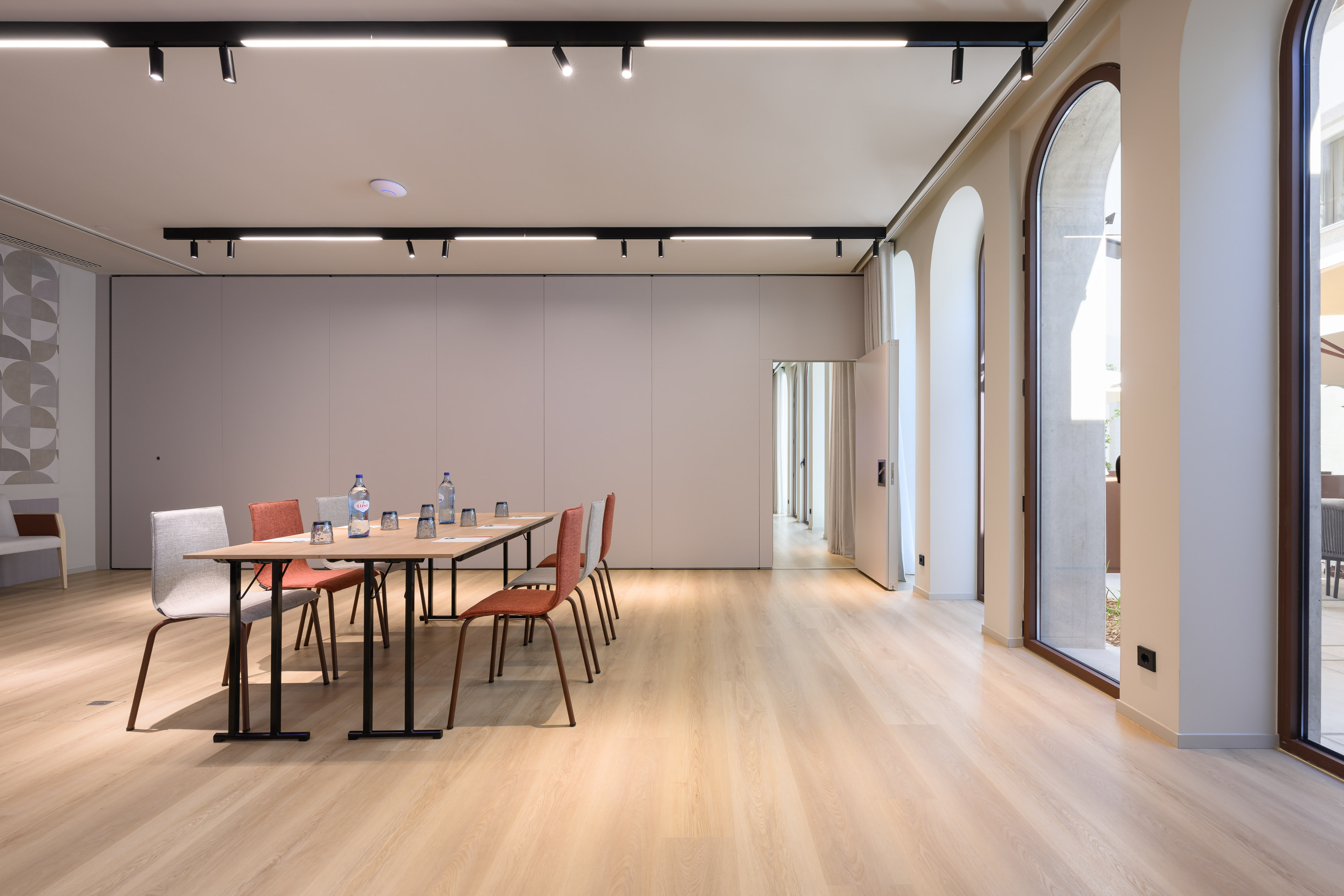 Modern conference room with wooden table, light wood floor, and arched windows.