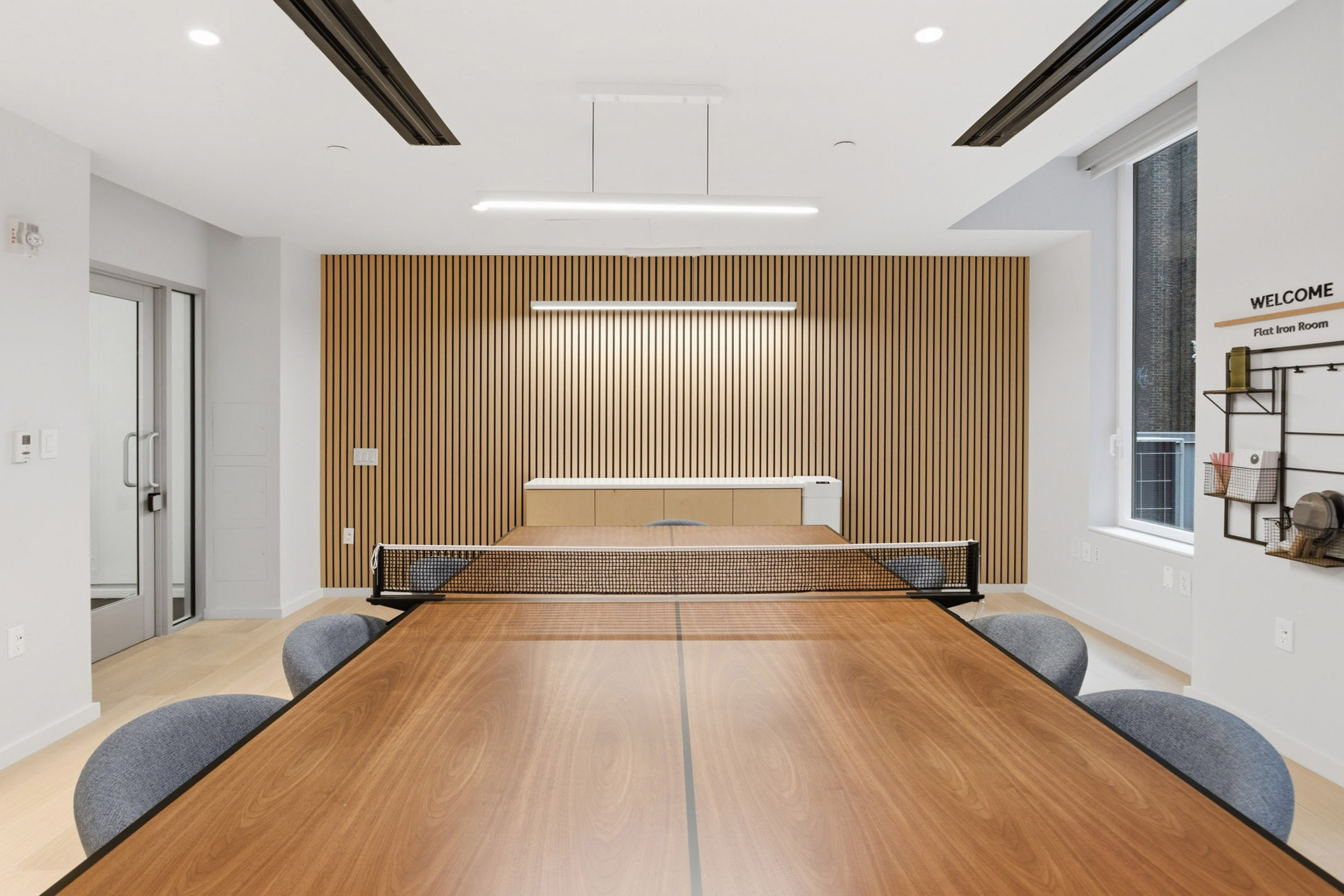Modern office game room with wooden ping pong table, slatted wall accent.