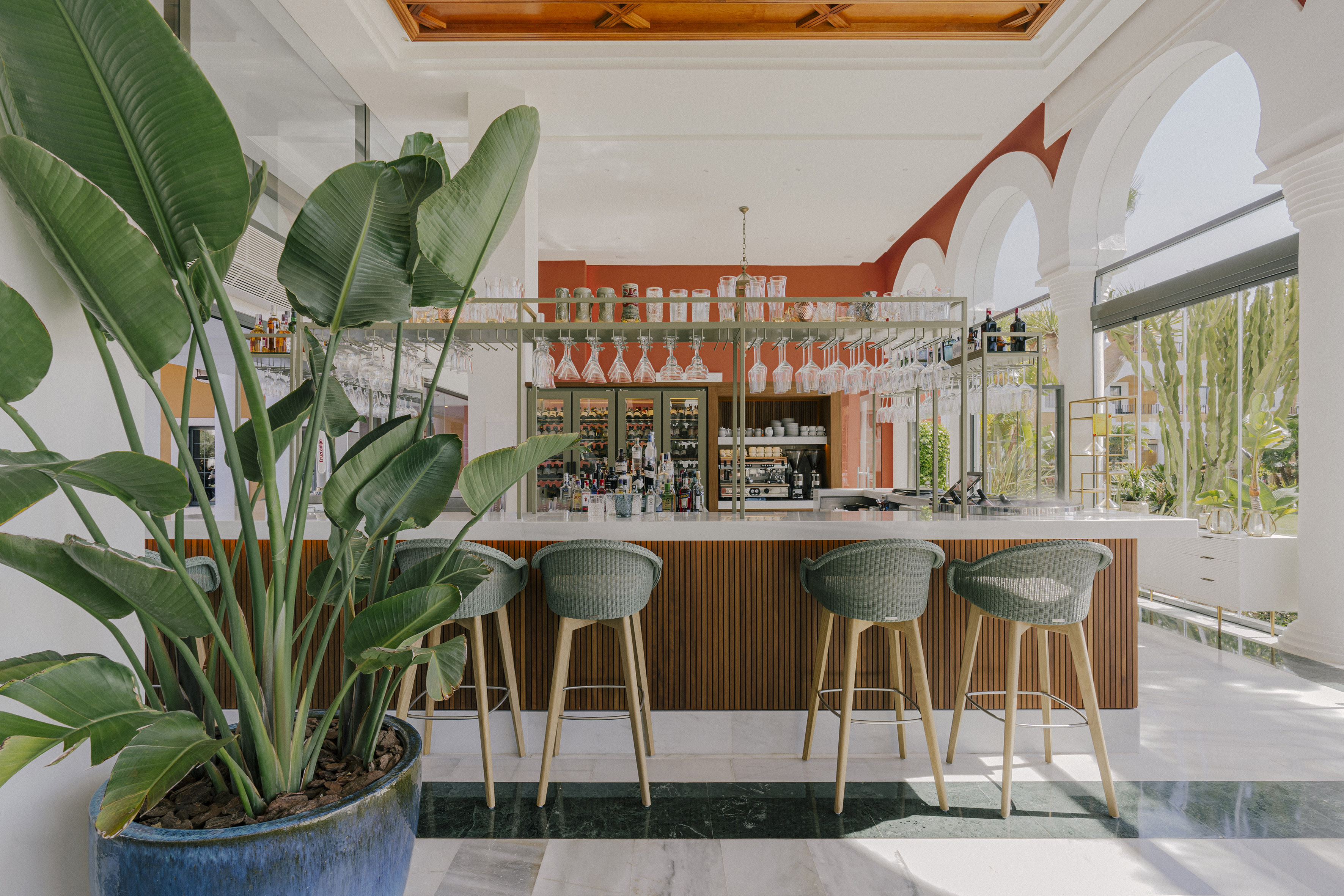 Modern resort bar with tropical plant, woven stools, and red walls.