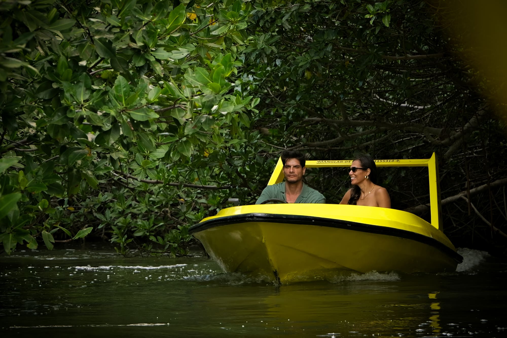 Hombre y mujer en bote amarillo explorando manglares.