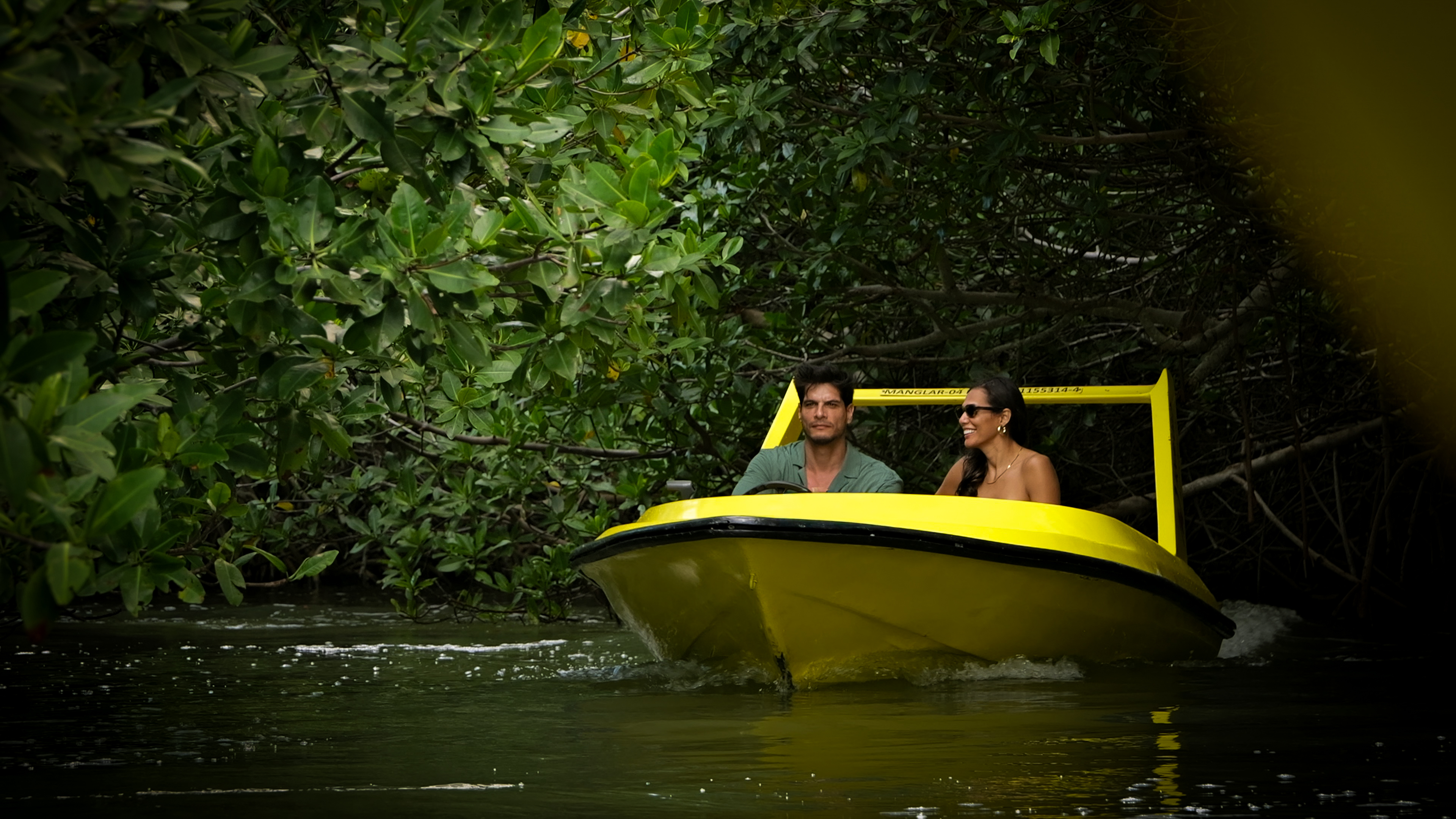 Hombre y mujer en bote amarillo explorando manglares.