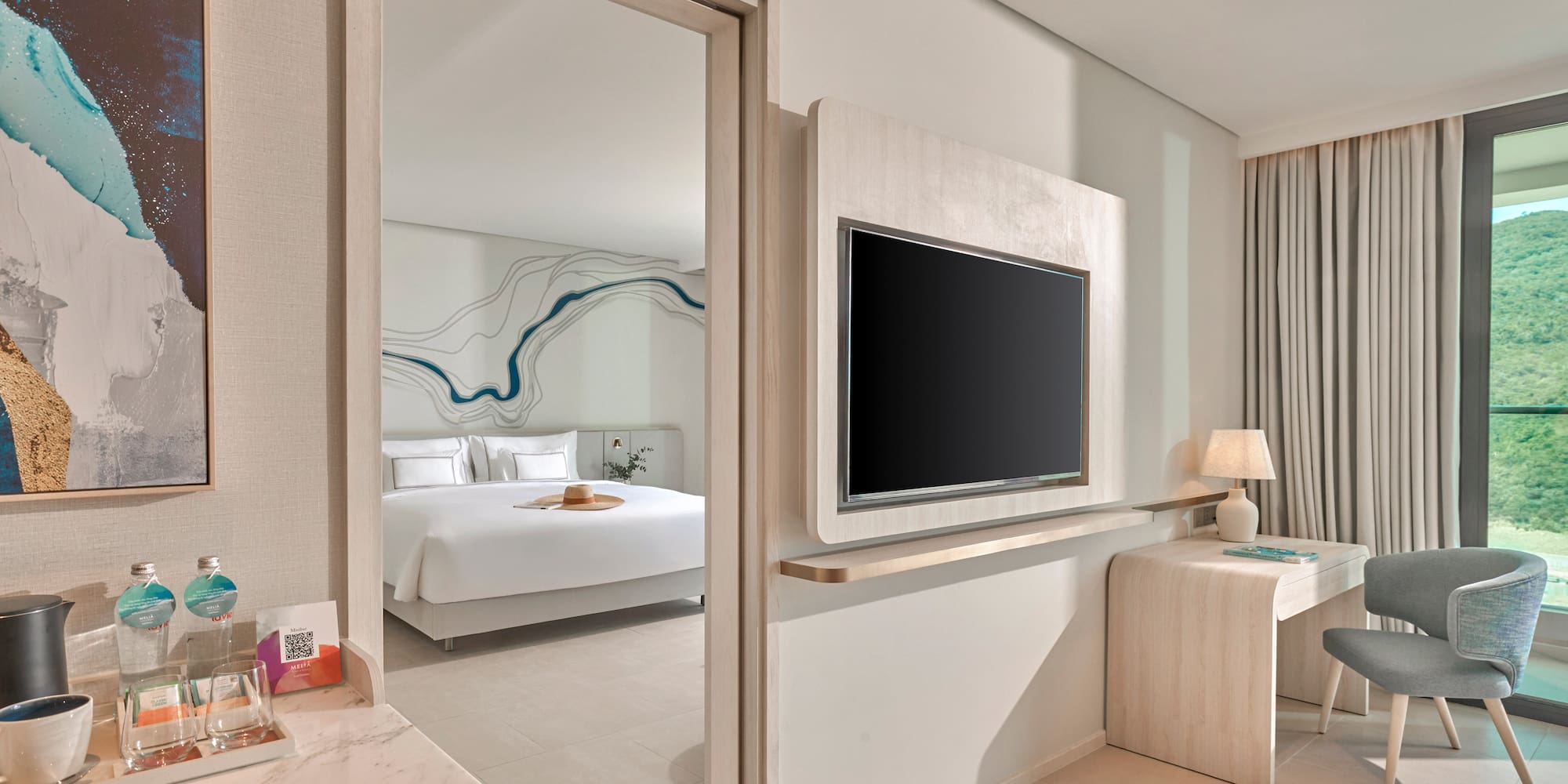 Modern hotel room with bedroom, wall TV, desk, and mountain view.