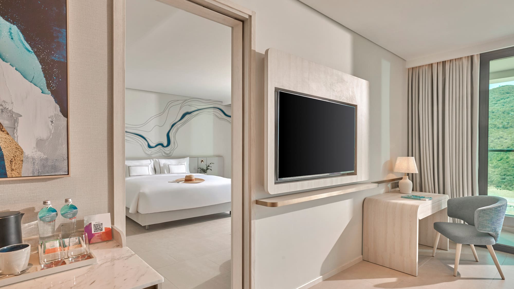 Modern hotel room with bedroom, wall TV, desk, and mountain view.