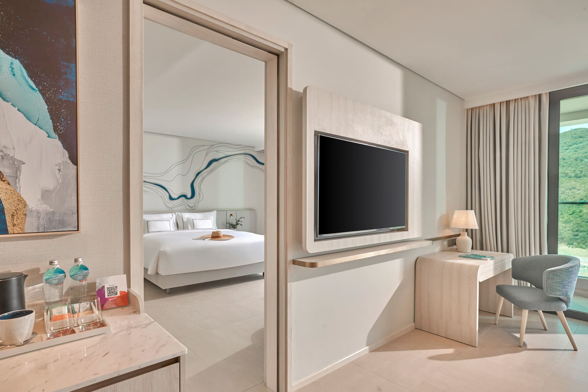 Modern hotel room with bedroom, wall TV, desk, and mountain view.