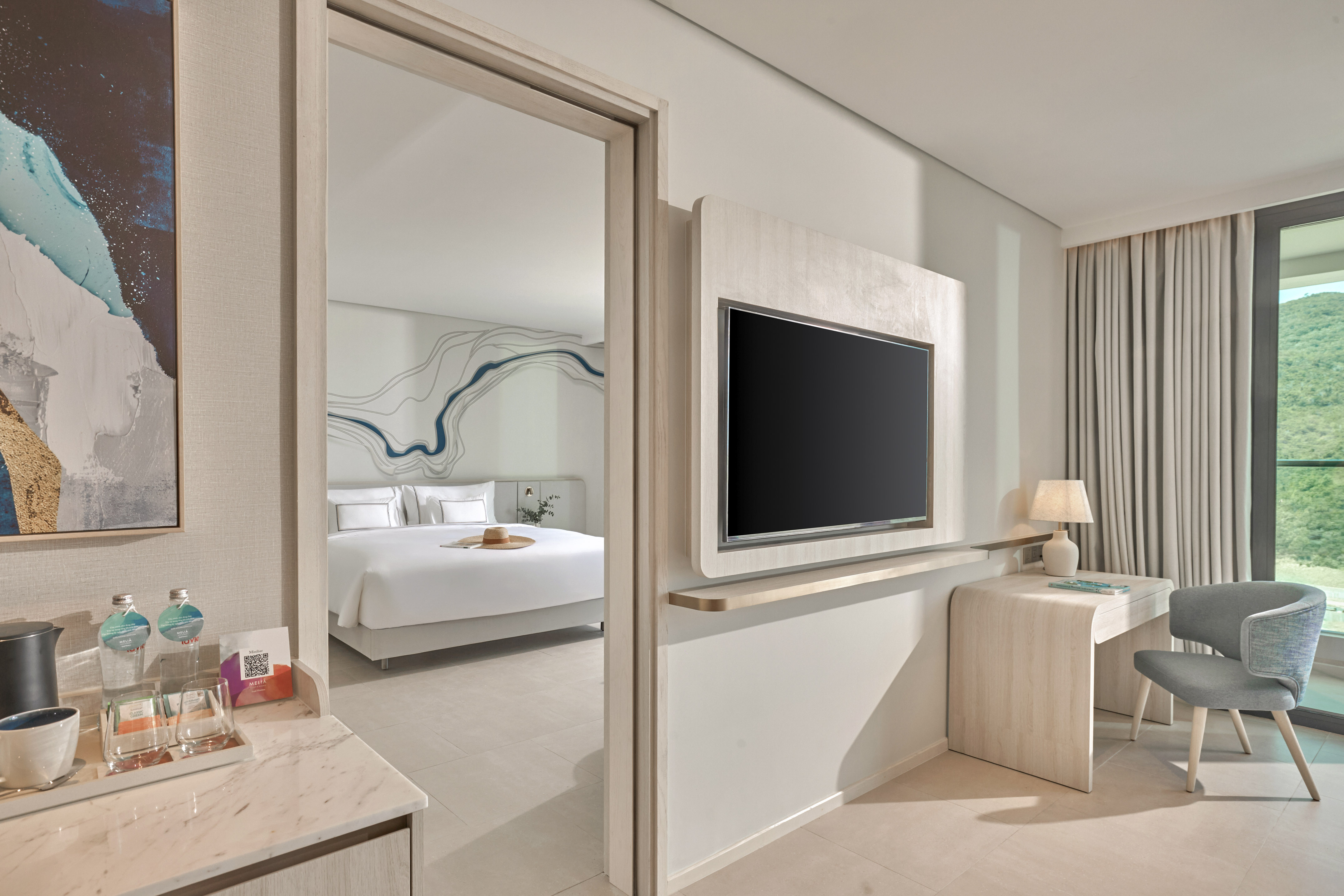 Modern hotel room with bedroom, wall TV, desk, and mountain view.
