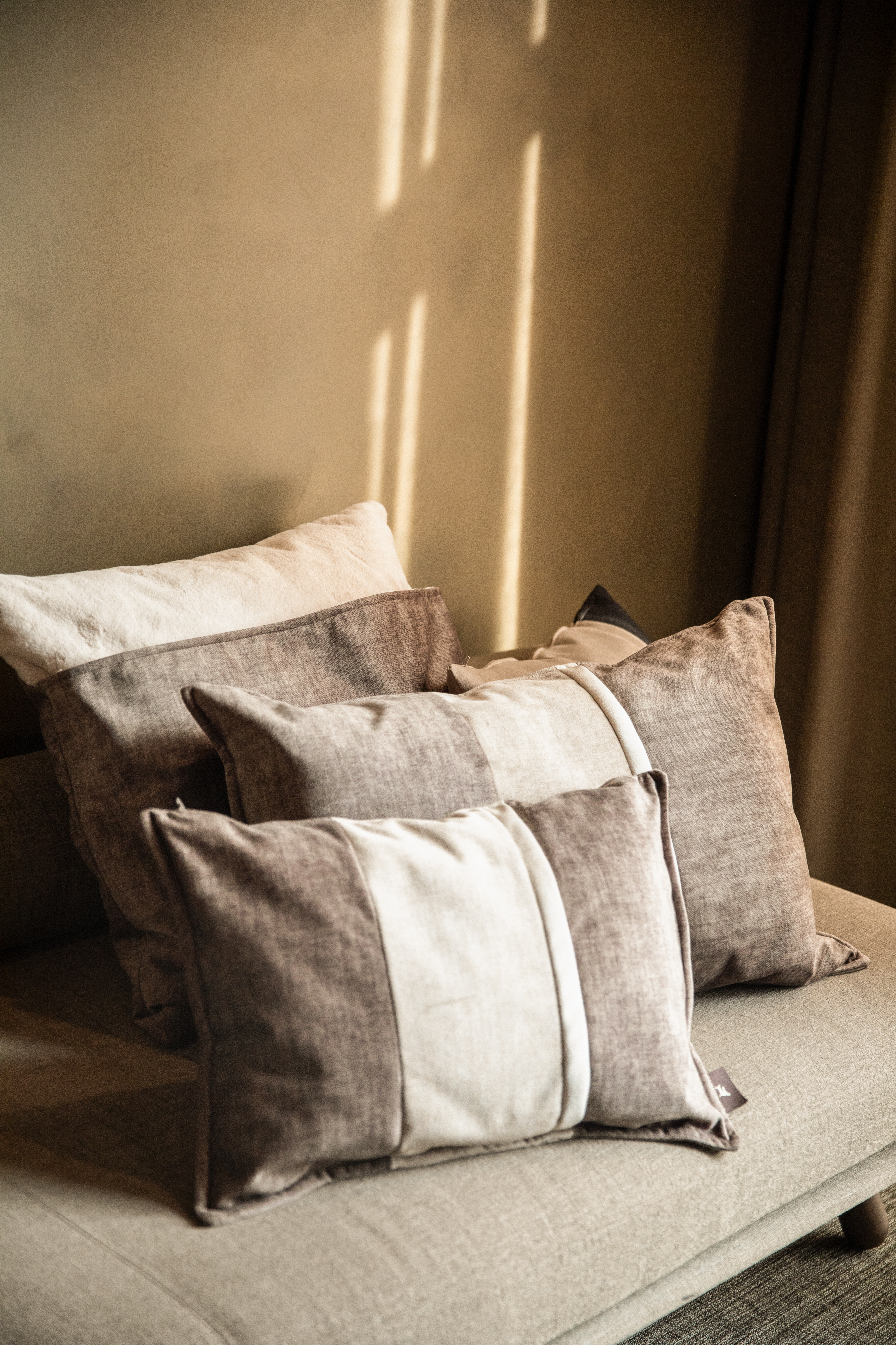 Brown and cream decorative pillows on a sofa, sunlit wall background.
