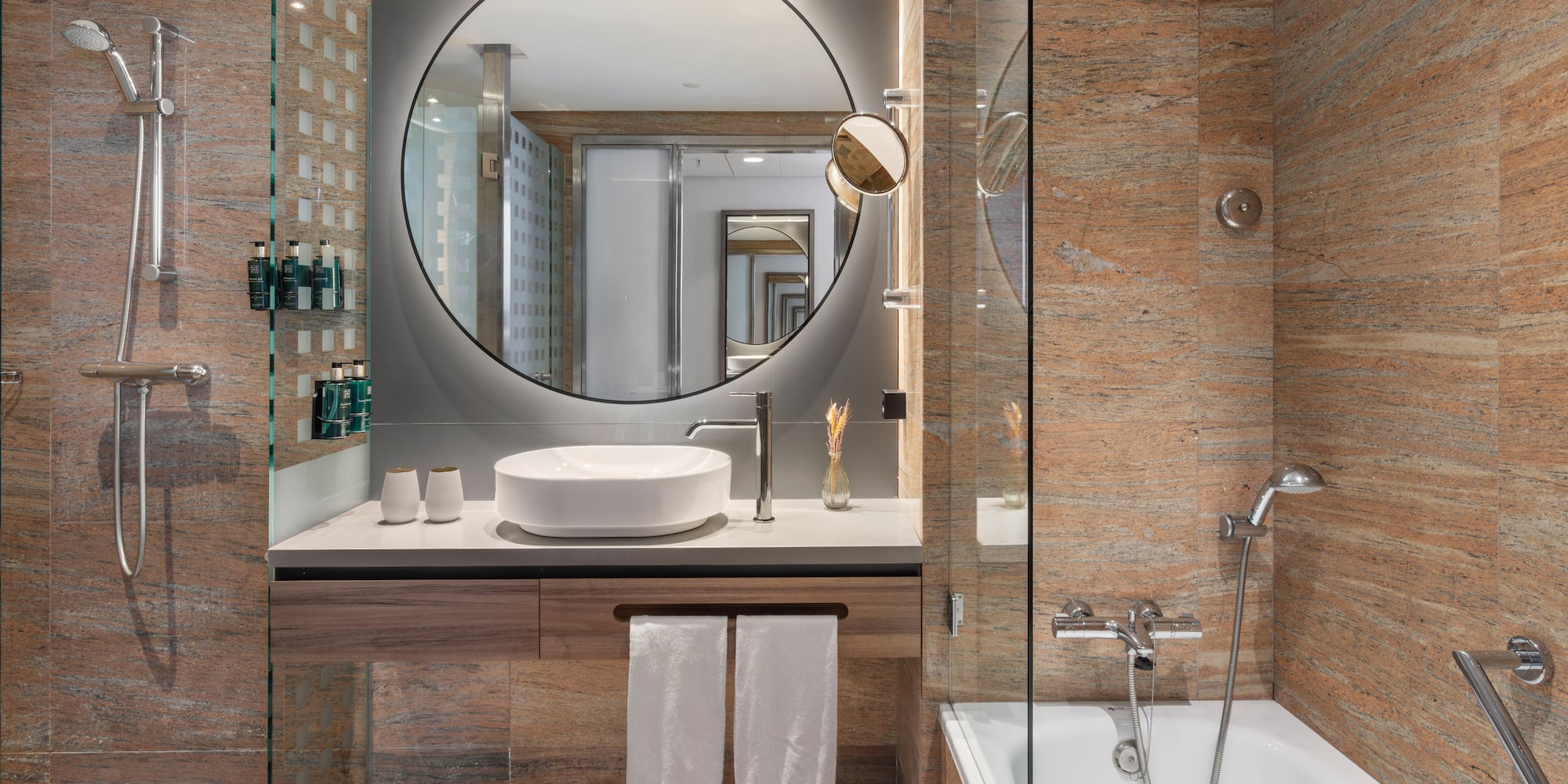 Baño moderno hotel. Ducha, bañera, lavabo, espejo y paredes de granito.