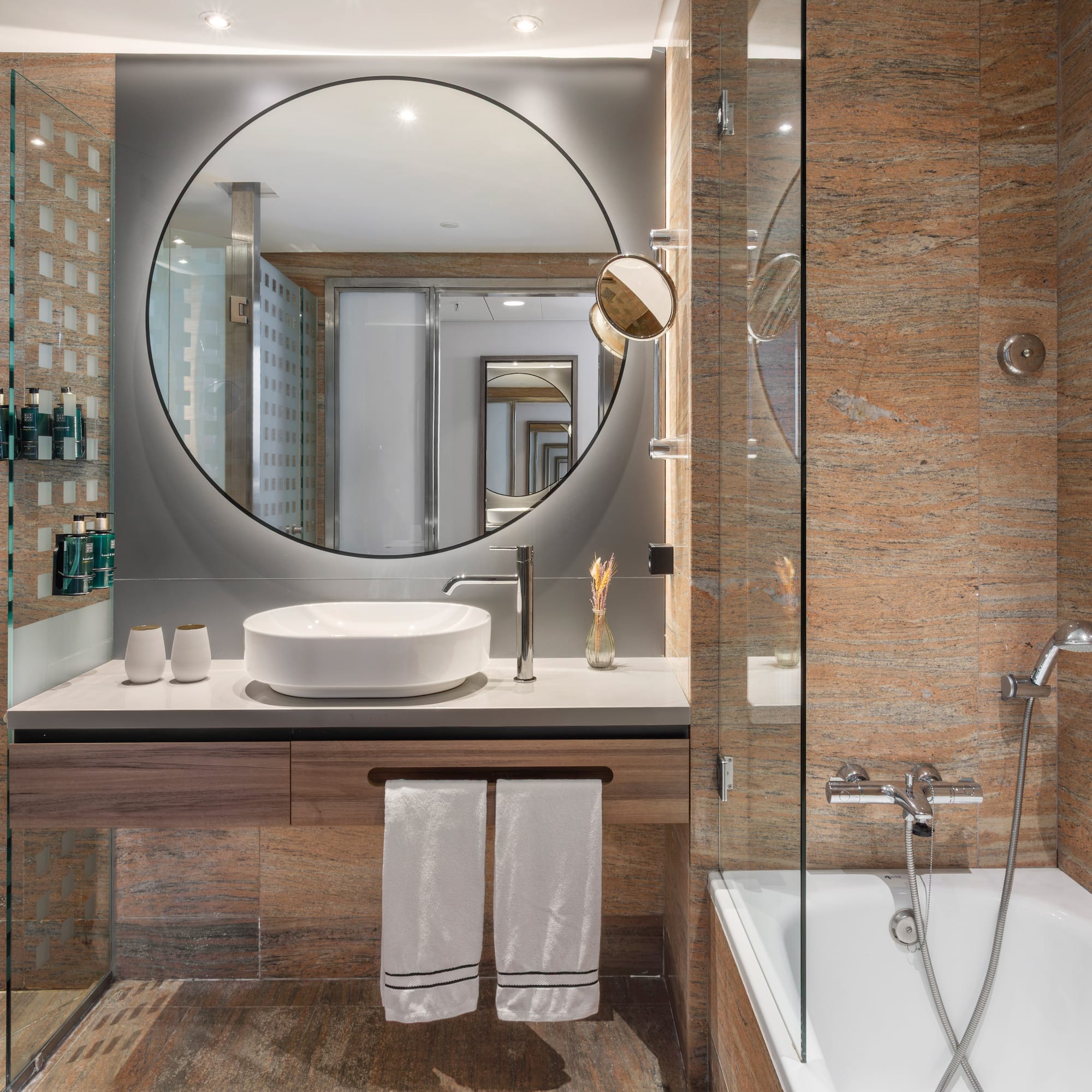 Baño moderno: ducha, bañera, lavabo, espejo redondo, mármol.
