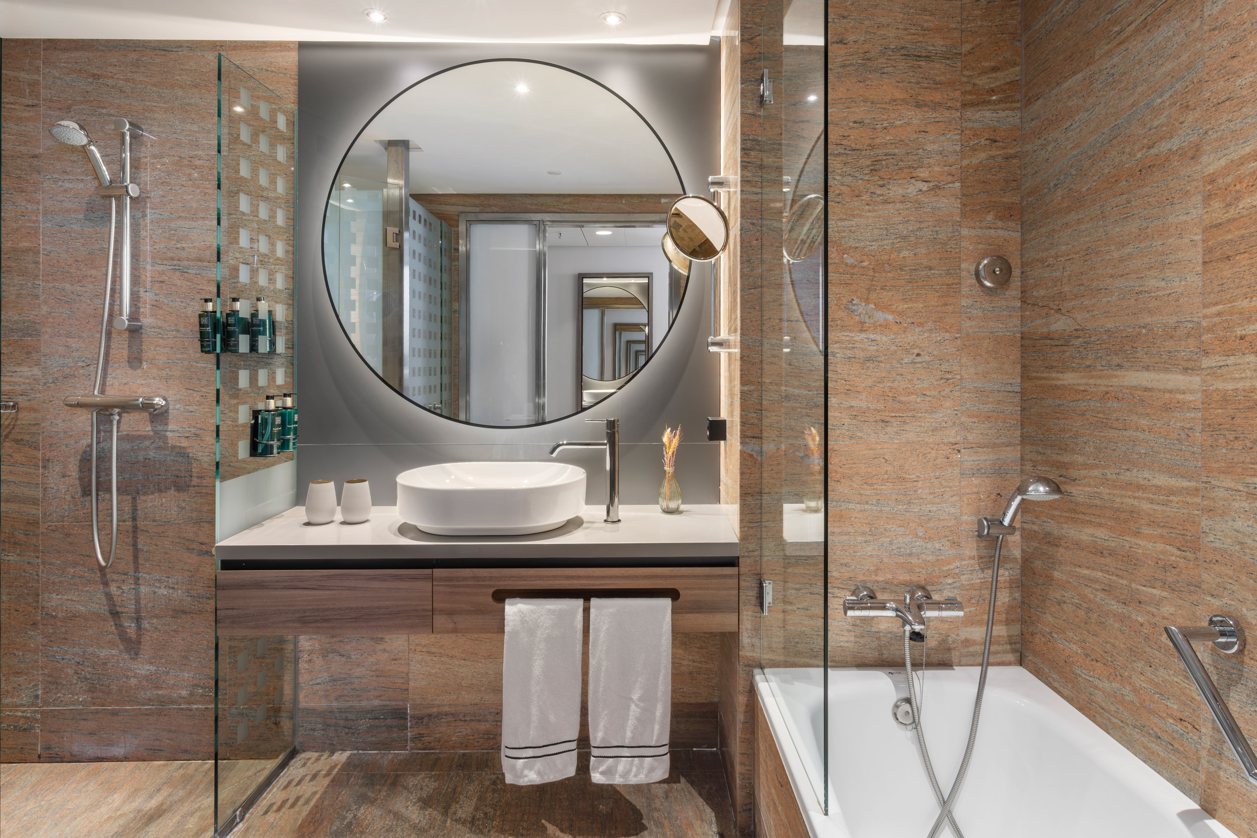 Baño moderno hotel. Ducha, bañera, lavabo, espejo y paredes de granito.