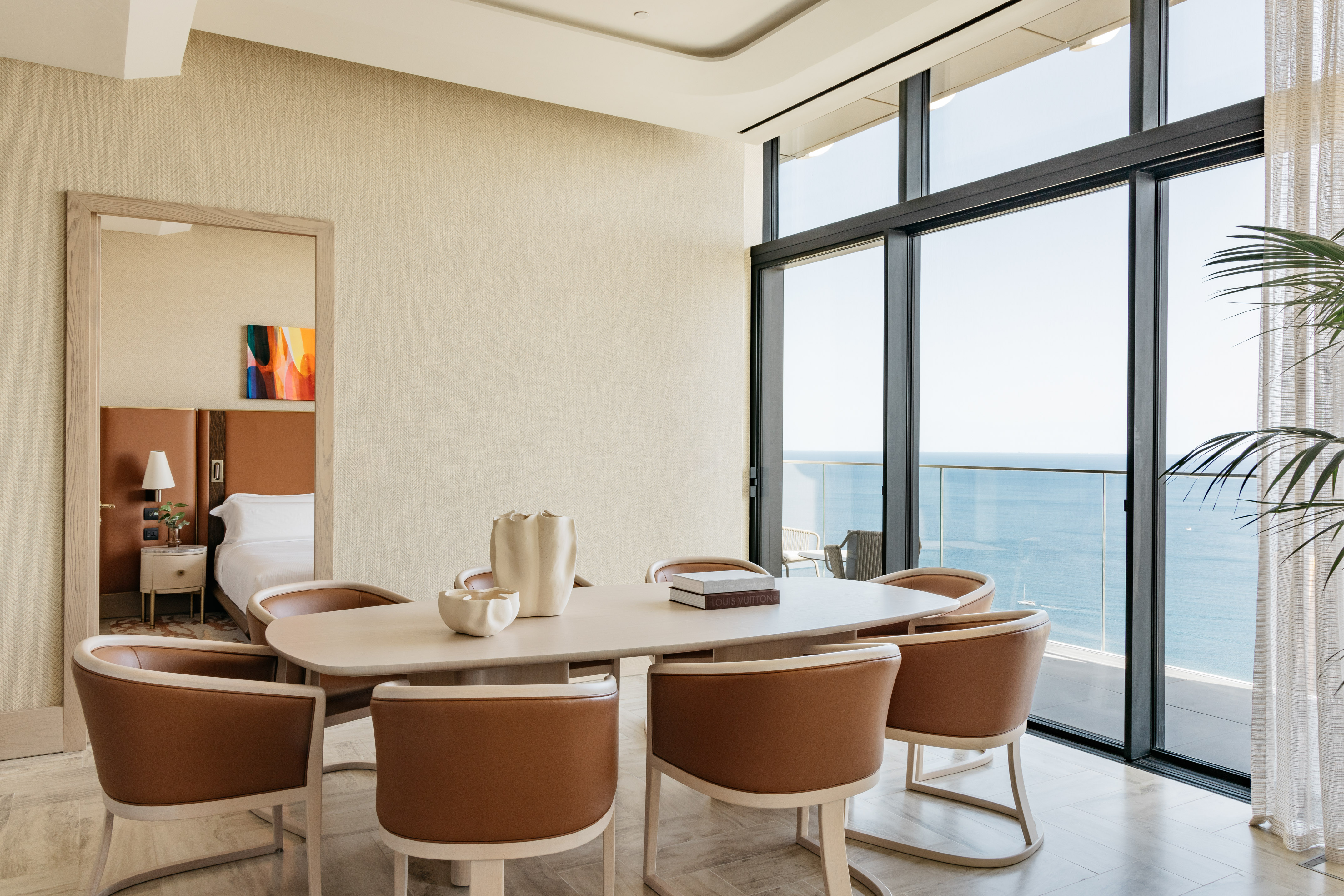 Modern dining room with ocean view, light wood table, and brown leather chairs.