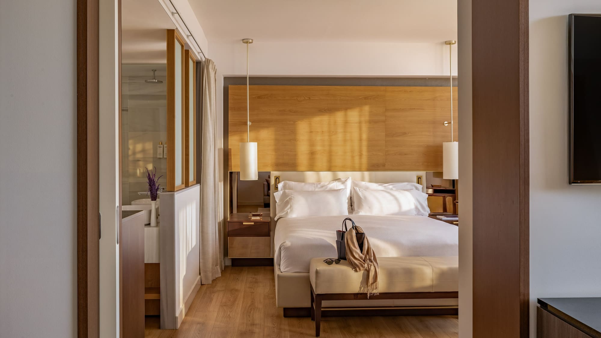 Sunlit modern hotel bedroom with king bed, wooden decor, and ensuite bath.