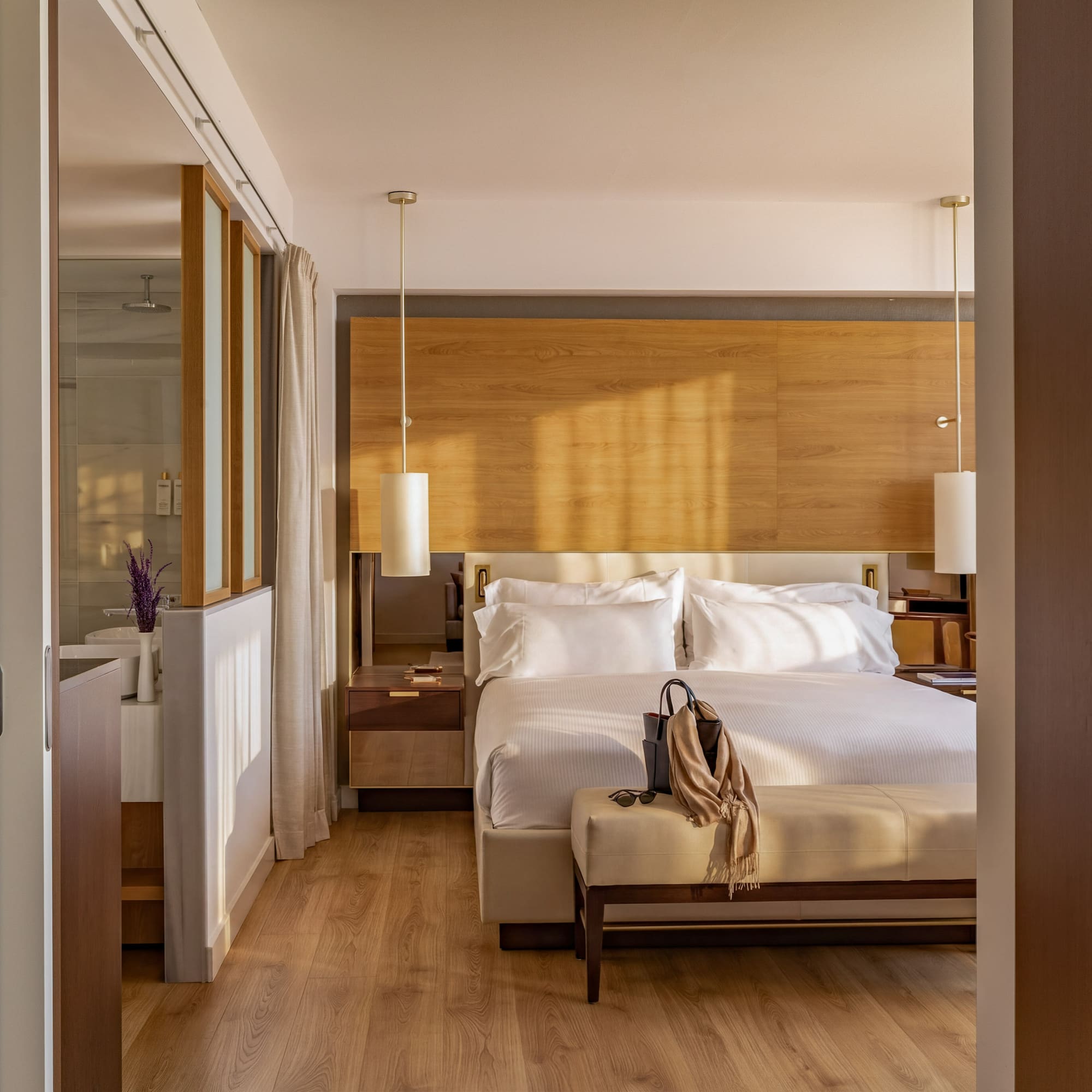 Sunlit modern hotel bedroom with king bed, wooden decor, and ensuite bath.