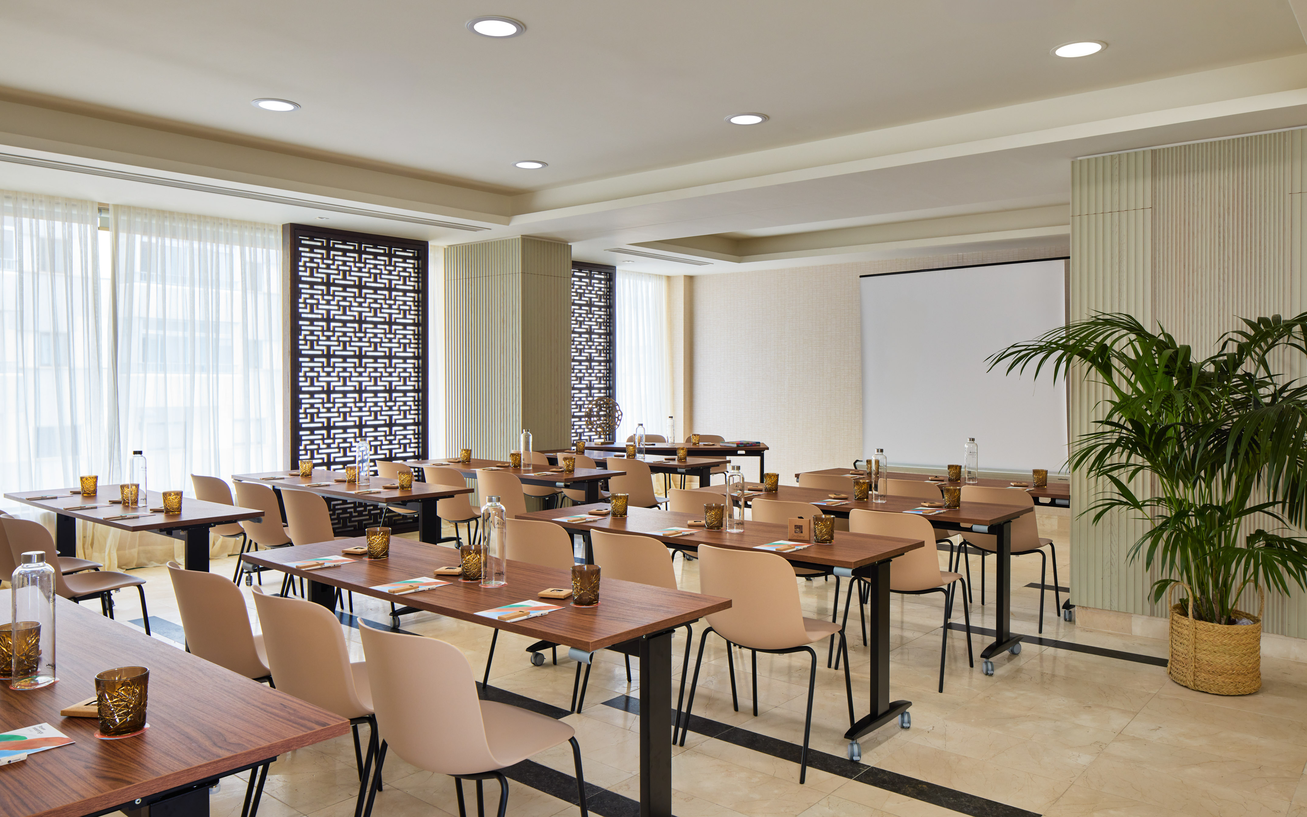 Modern conference room with tables, beige chairs, and large presentation screen.