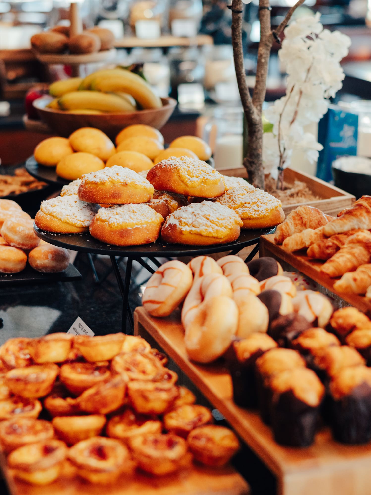 Breakfast buffet with donuts, croissants, muffins, tarts, and fresh fruit.