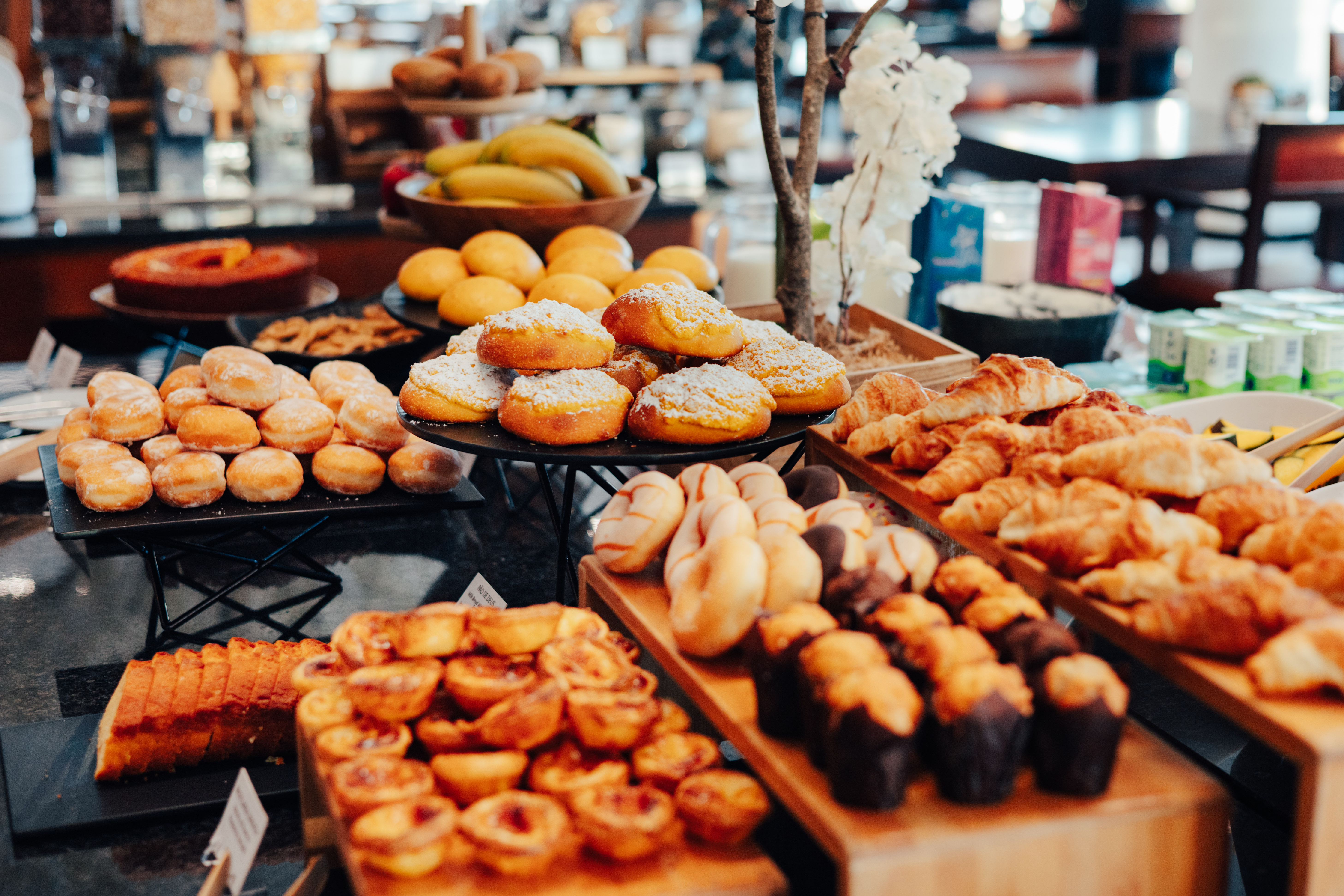Breakfast buffet with donuts, croissants, muffins, tarts, and fresh fruit.