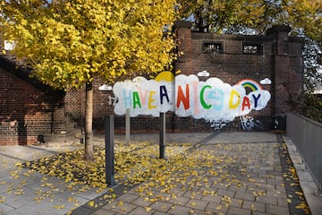a sign with a cloud and rainbow in front of a brick wall