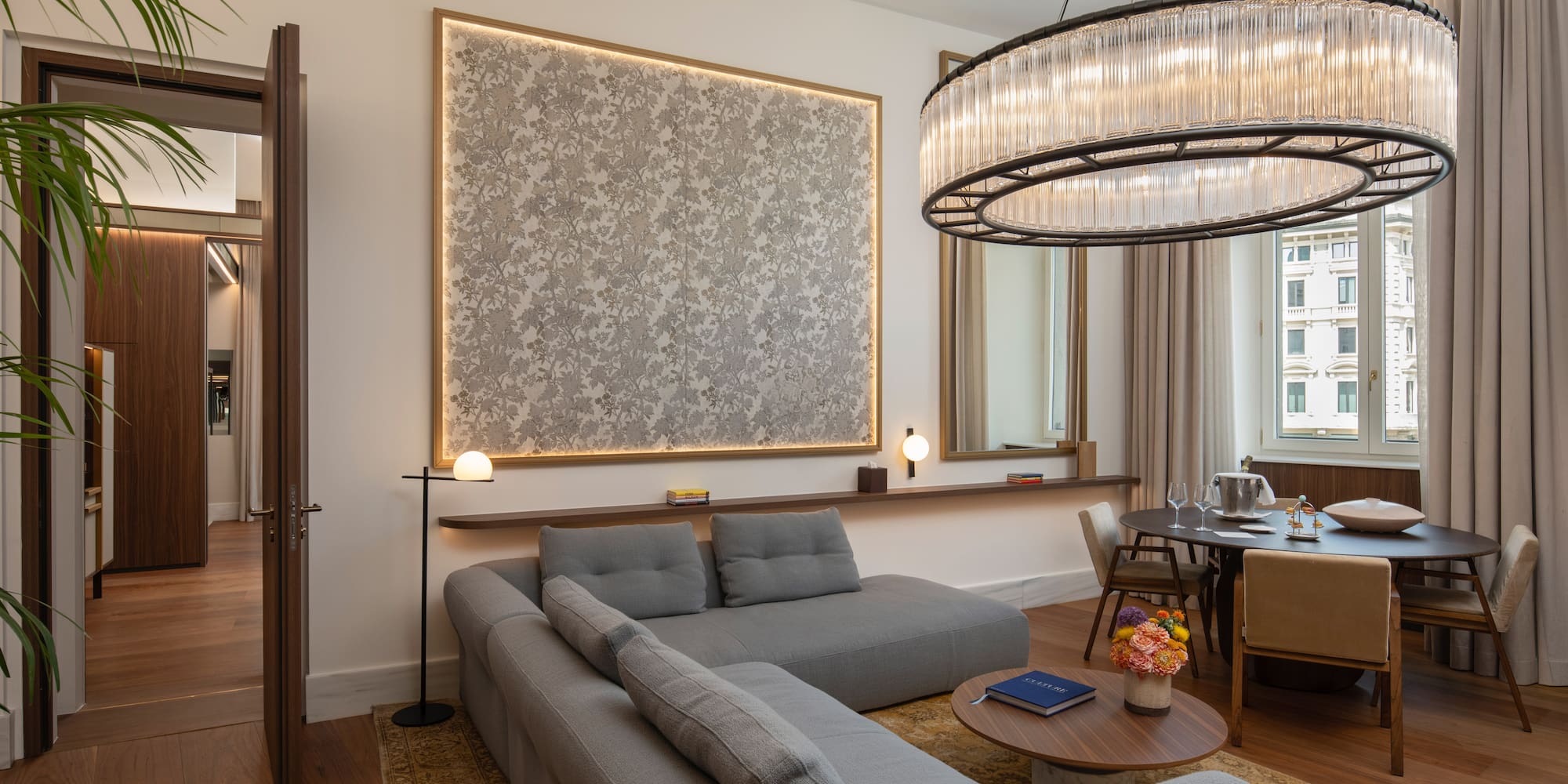Modern luxury living room with grey sofa, dining table, and stunning chandelier.