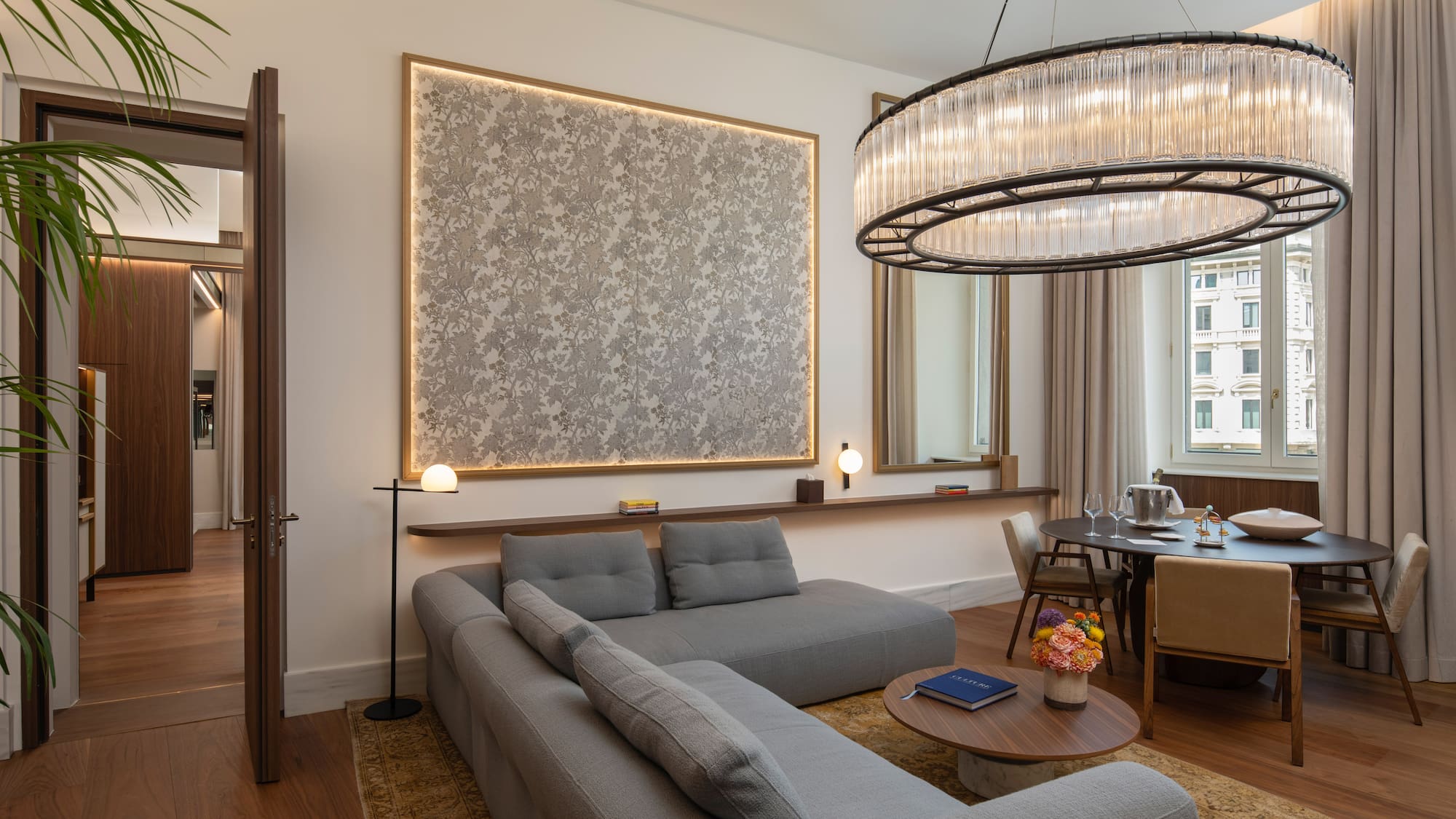 Modern luxury living room with grey sofa, dining table, and stunning chandelier.