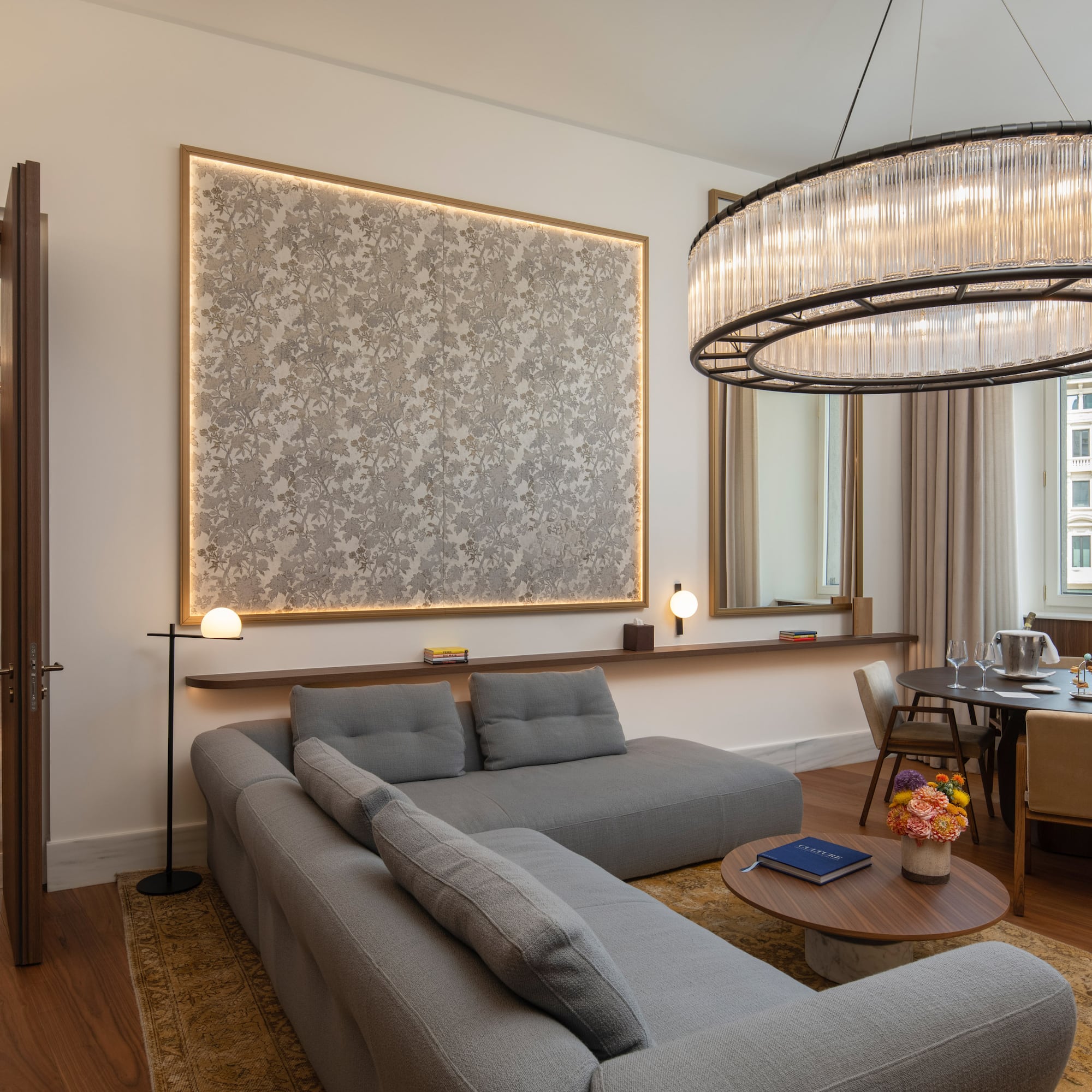 Modern luxury living room with grey sofa, dining table, and stunning chandelier.