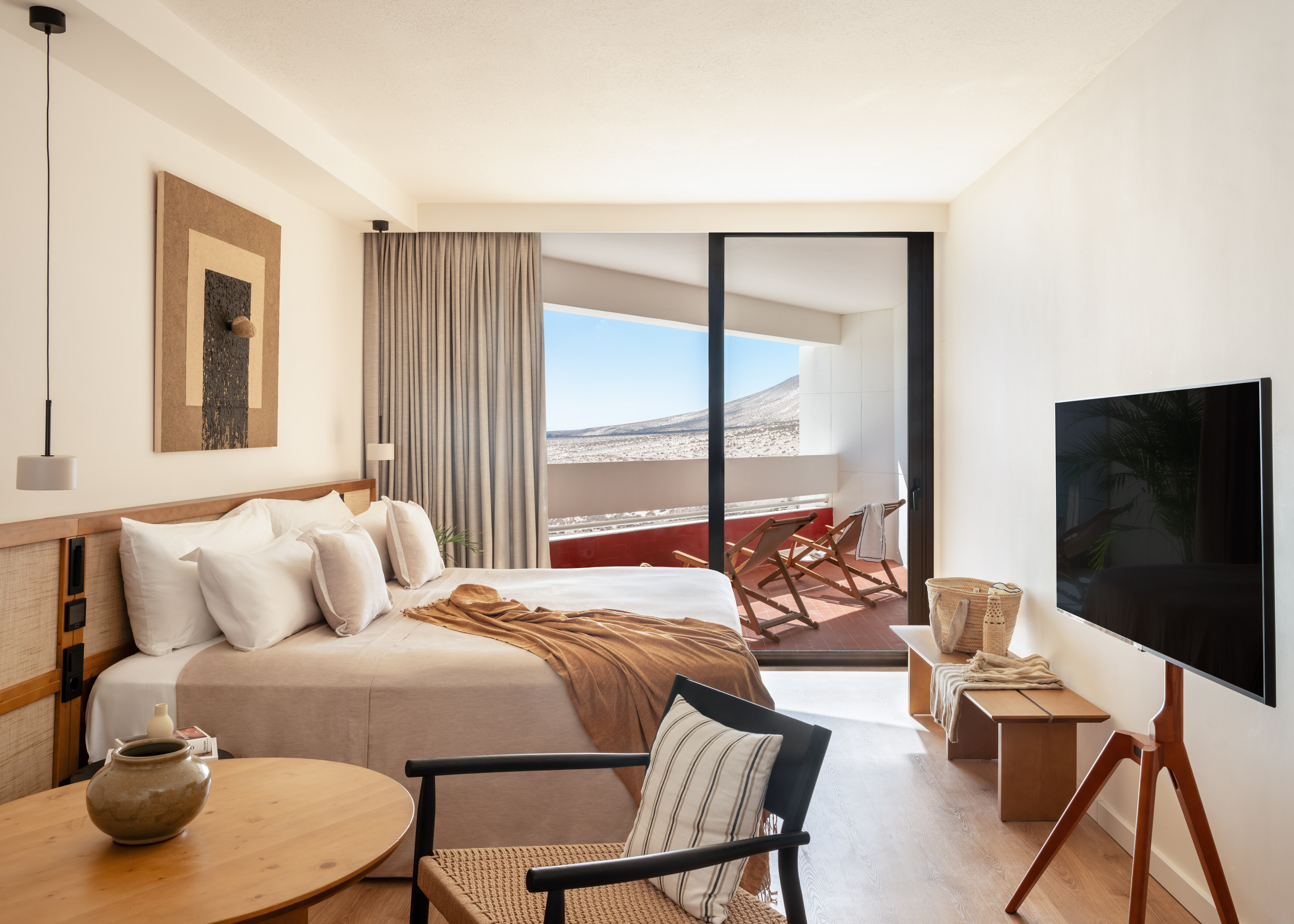 Modern hotel bedroom with desert view balcony, king bed, and natural wood decor.