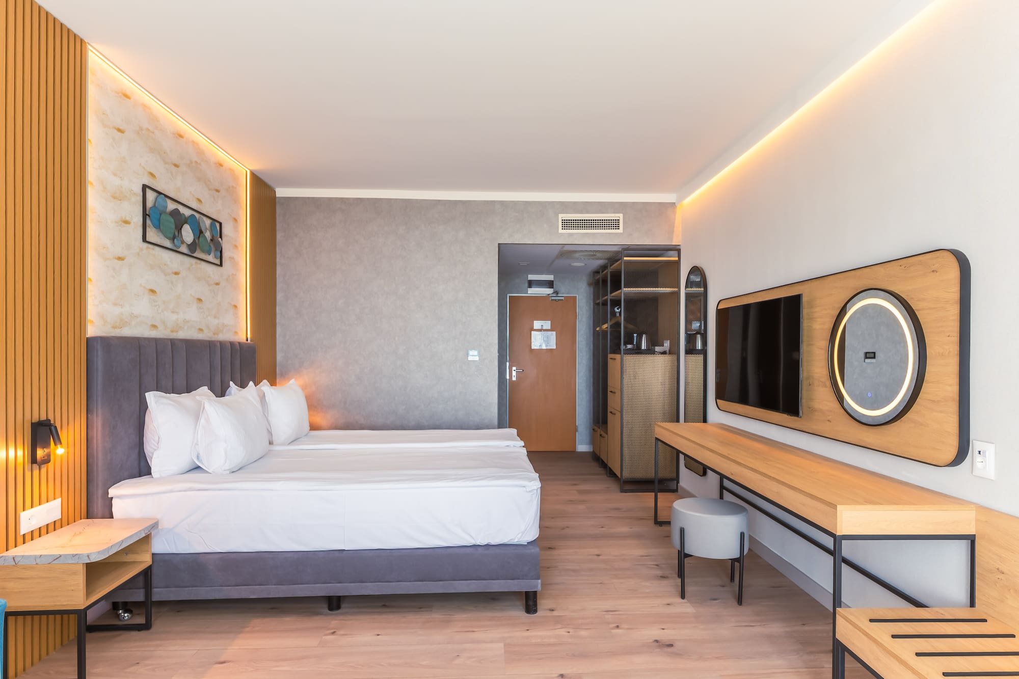 Modern hotel room with bed, wood floor, ambient lighting, TV, and vanity.