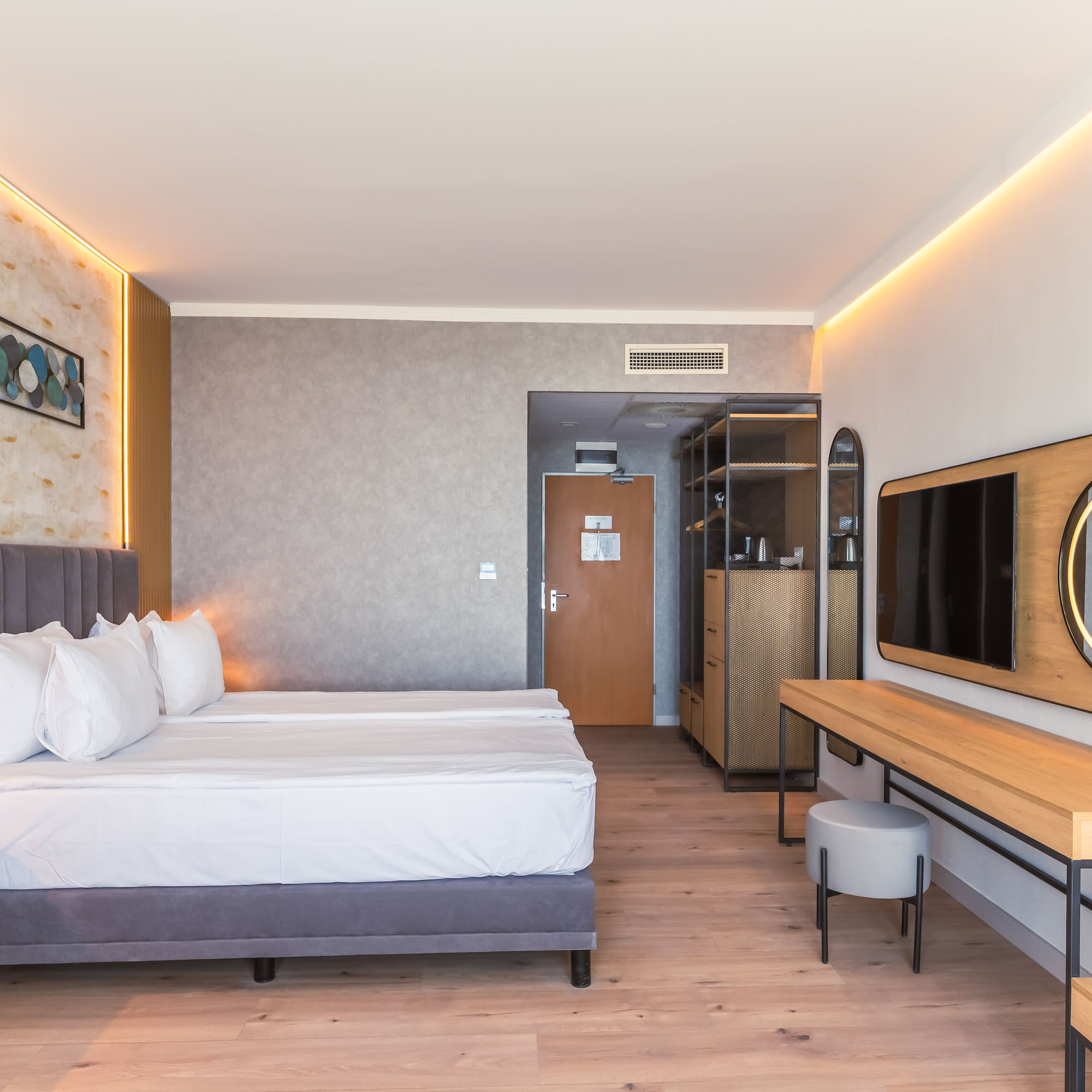Modern hotel room with bed, wood floor, ambient lighting, TV, and vanity.