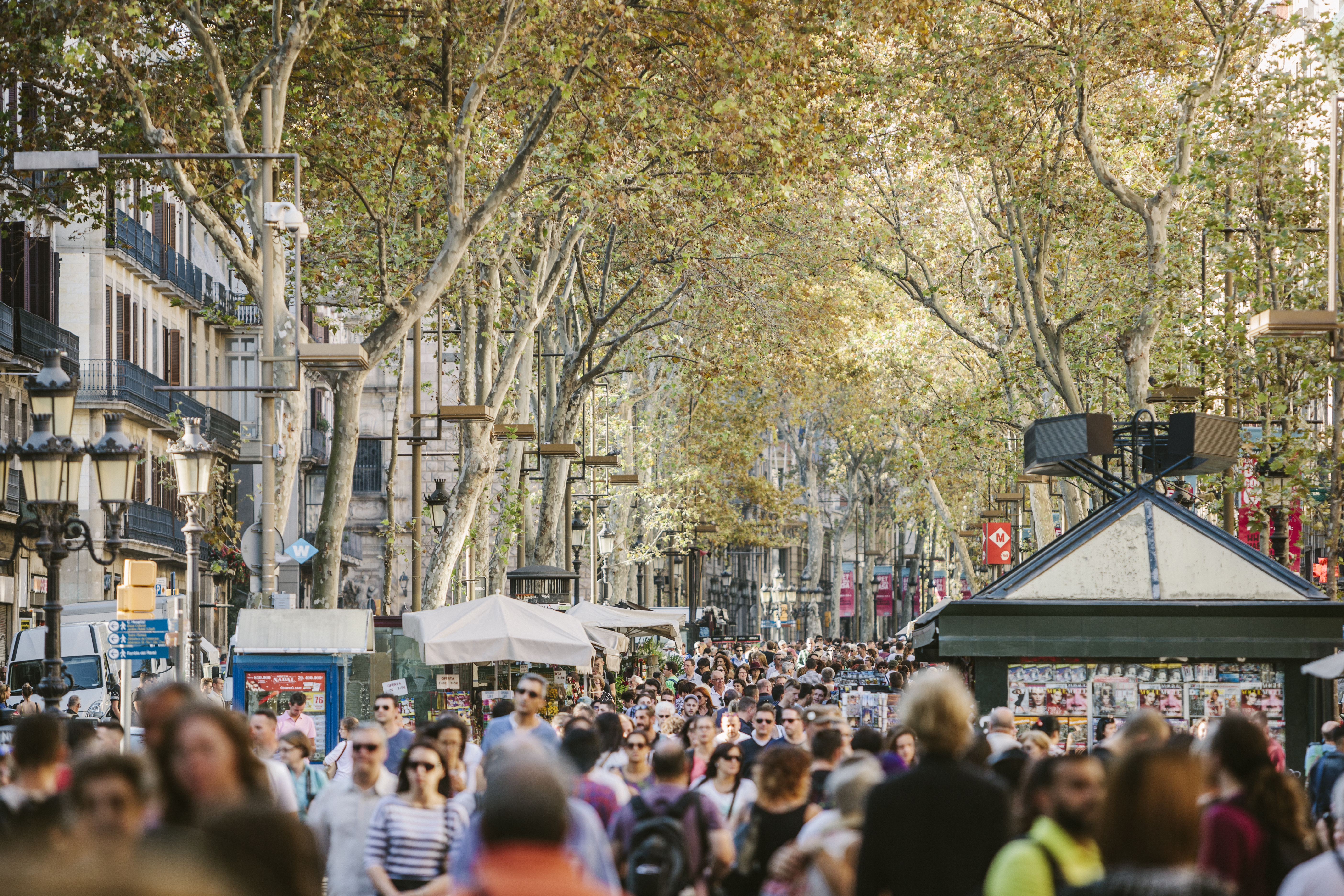 Paseo concurrido en La Rambla, Barcelona, con árboles otoñales y quioscos.