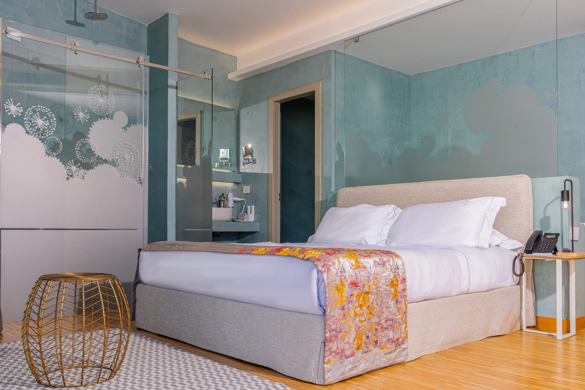 Modern hotel bedroom with large bed, teal walls, and frosted glass shower.