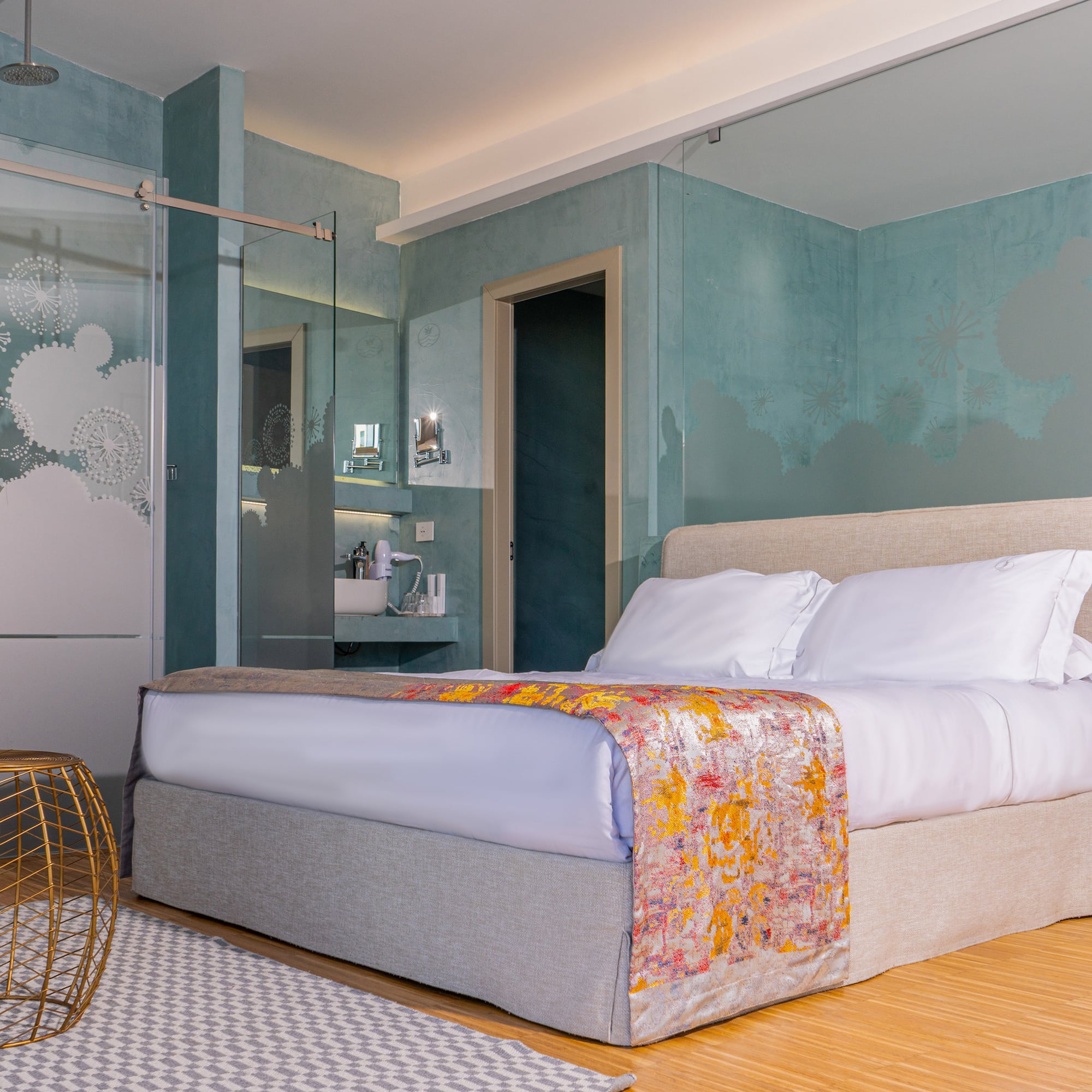 Modern hotel bedroom with large bed, teal walls, and frosted glass shower.