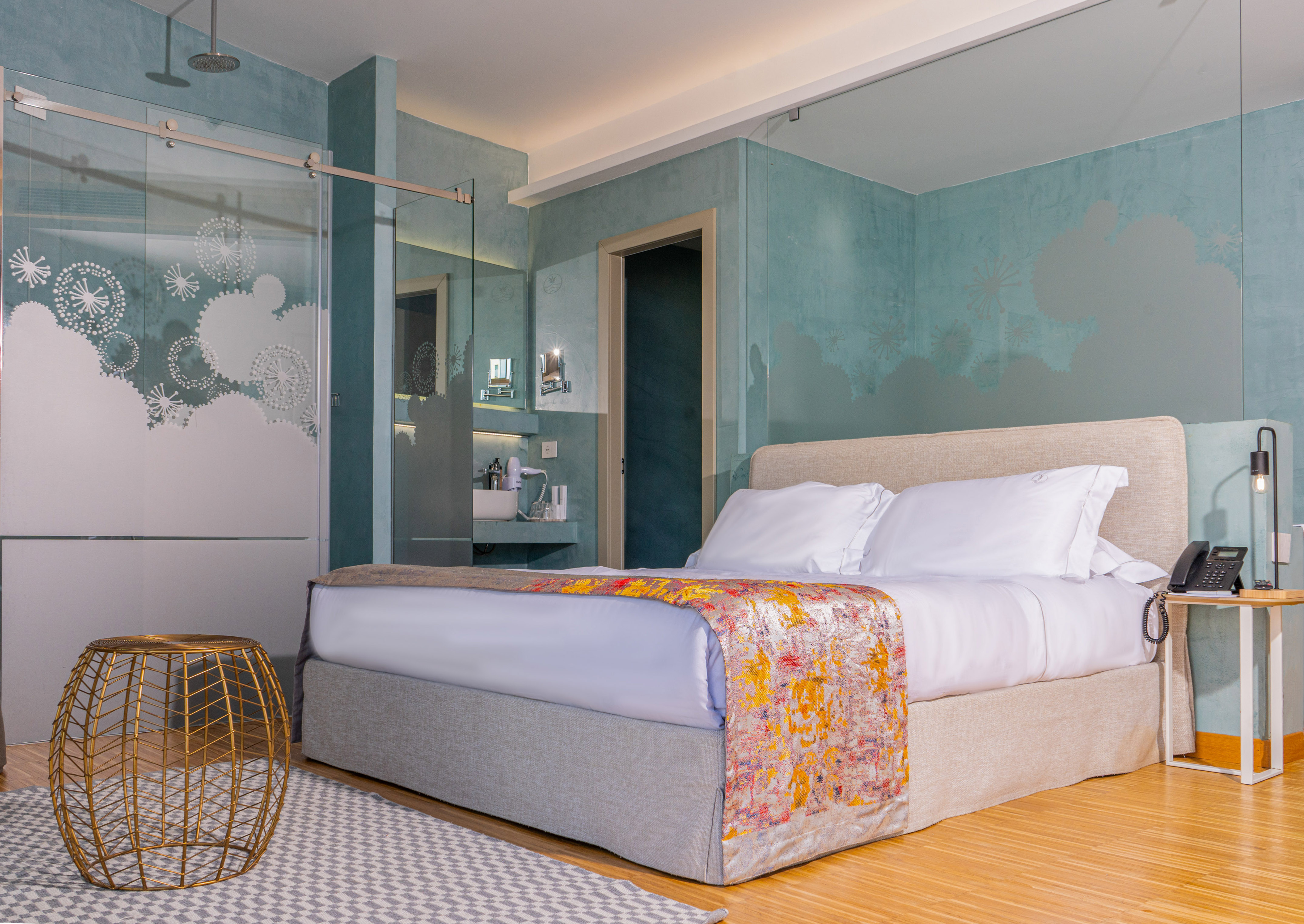 Modern hotel bedroom with large bed, teal walls, and frosted glass shower.
