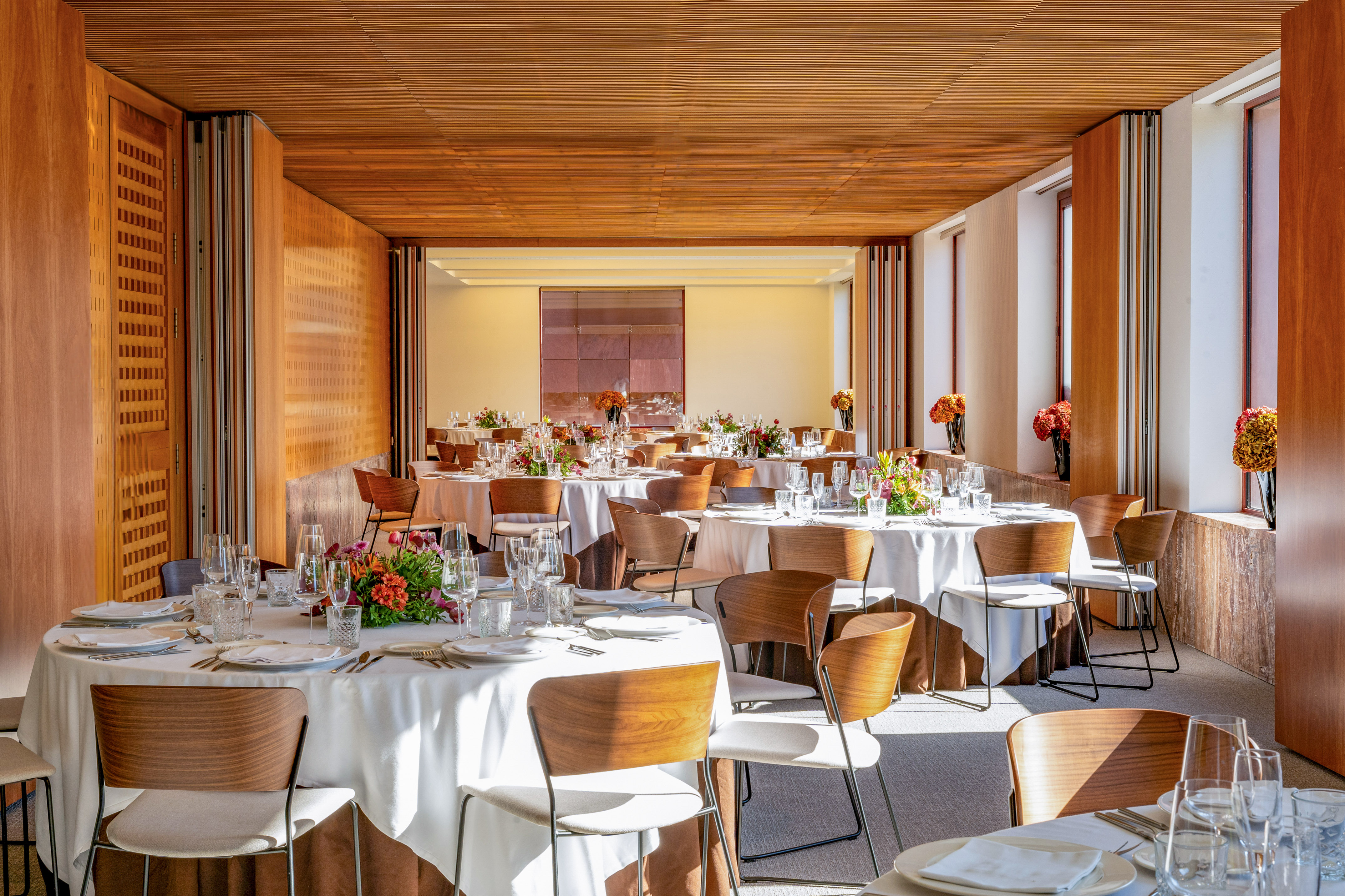 Modern banquet hall with set tables, floral arrangements, and warm wooden interior.