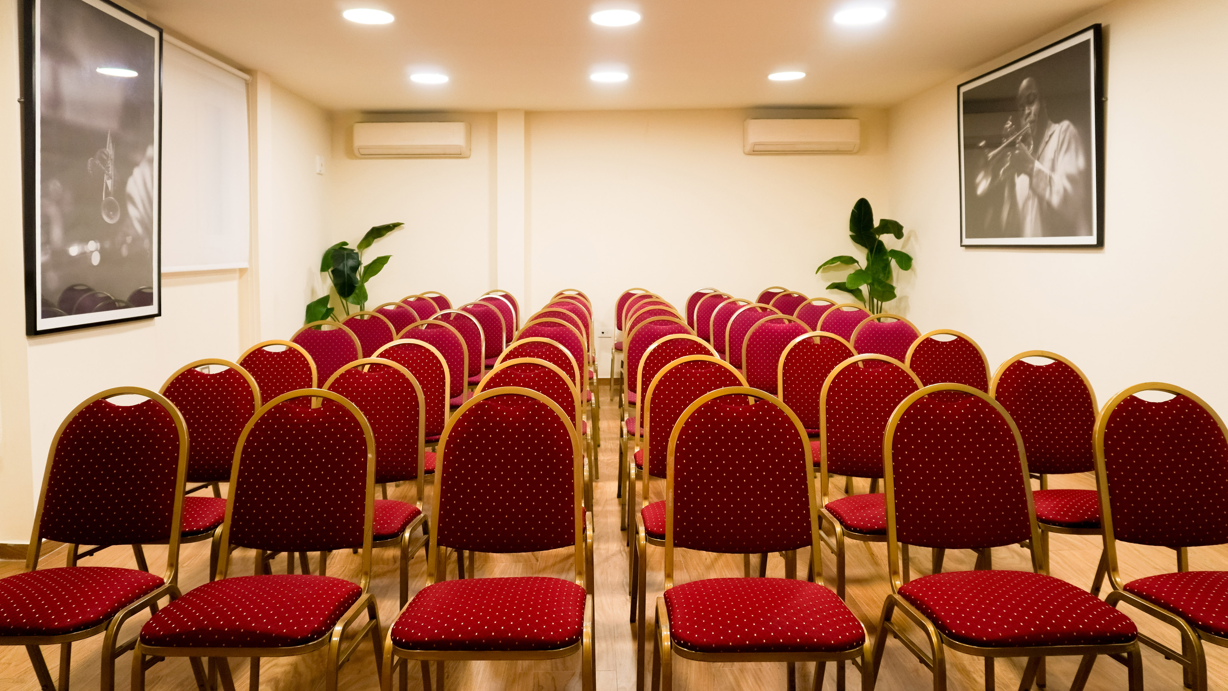 Empty conference room with rows of red and gold chairs, white walls, and jazz art. - Mallorca - Melia Recoleta Plaza, Buenos Aires