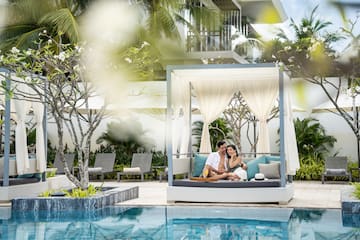 a man and woman sitting on a couch by a pool