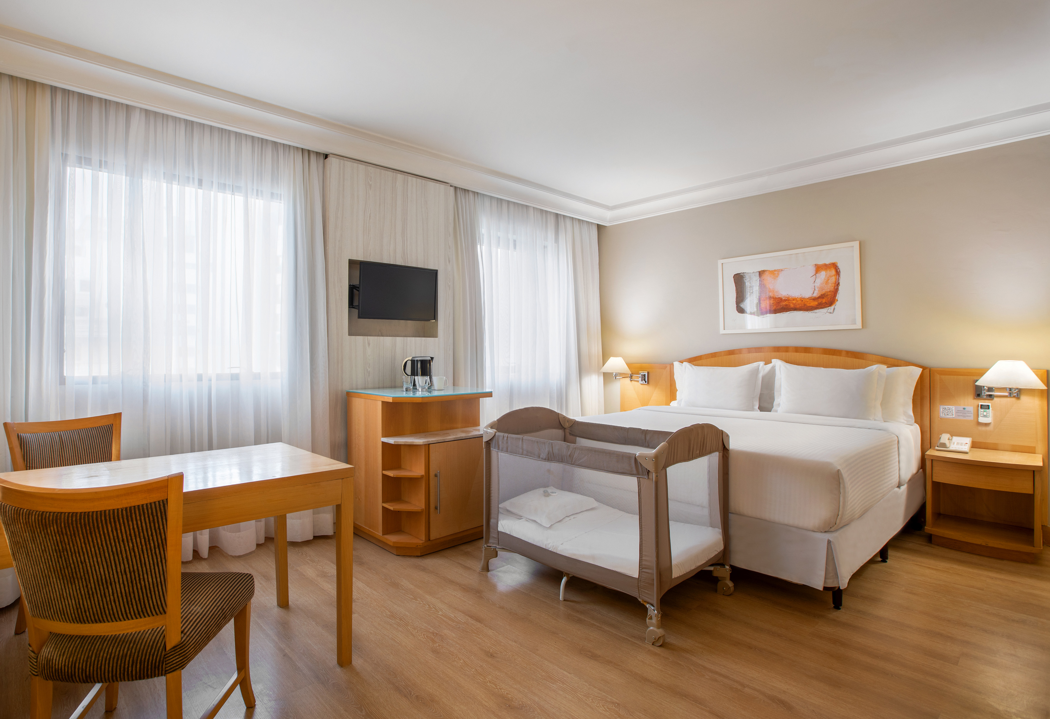 Modern hotel room with king bed, pack n play, dining area, and TV.
