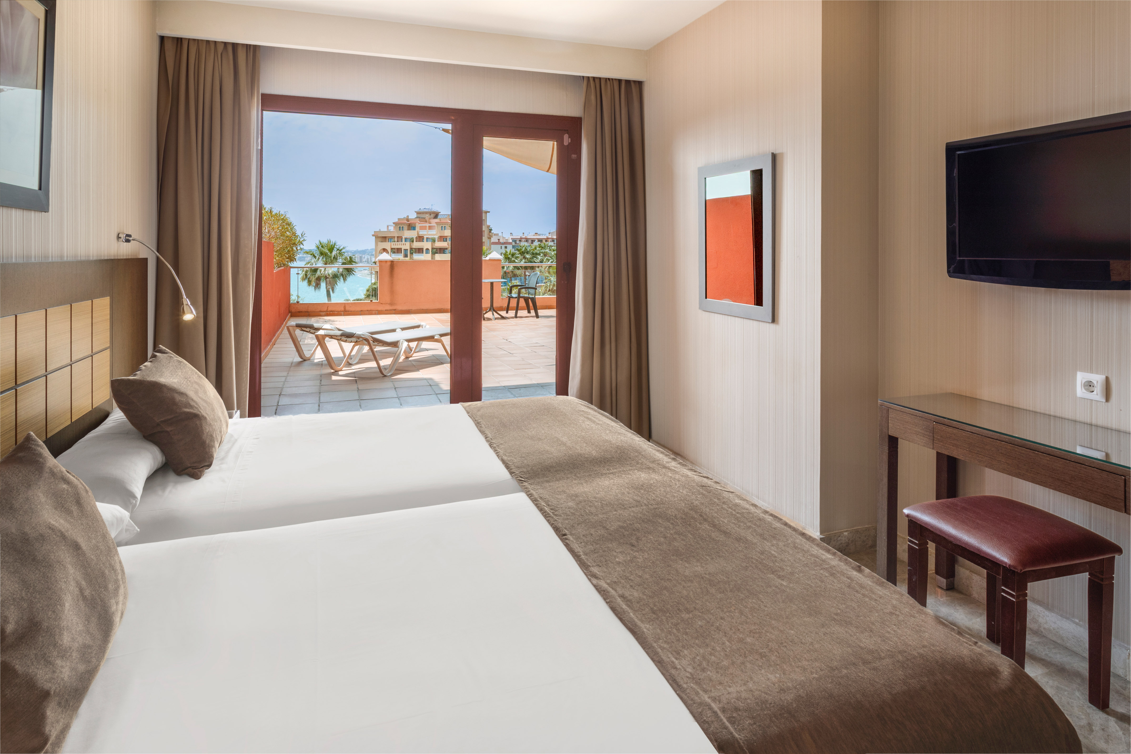 Resort hotel room with twin beds, private balcony, and ocean view.
