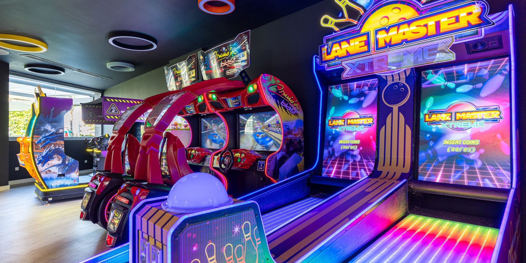 Neon-lit arcade with Lane Master Xtreme bowling and Cruis'n Blast racing games.