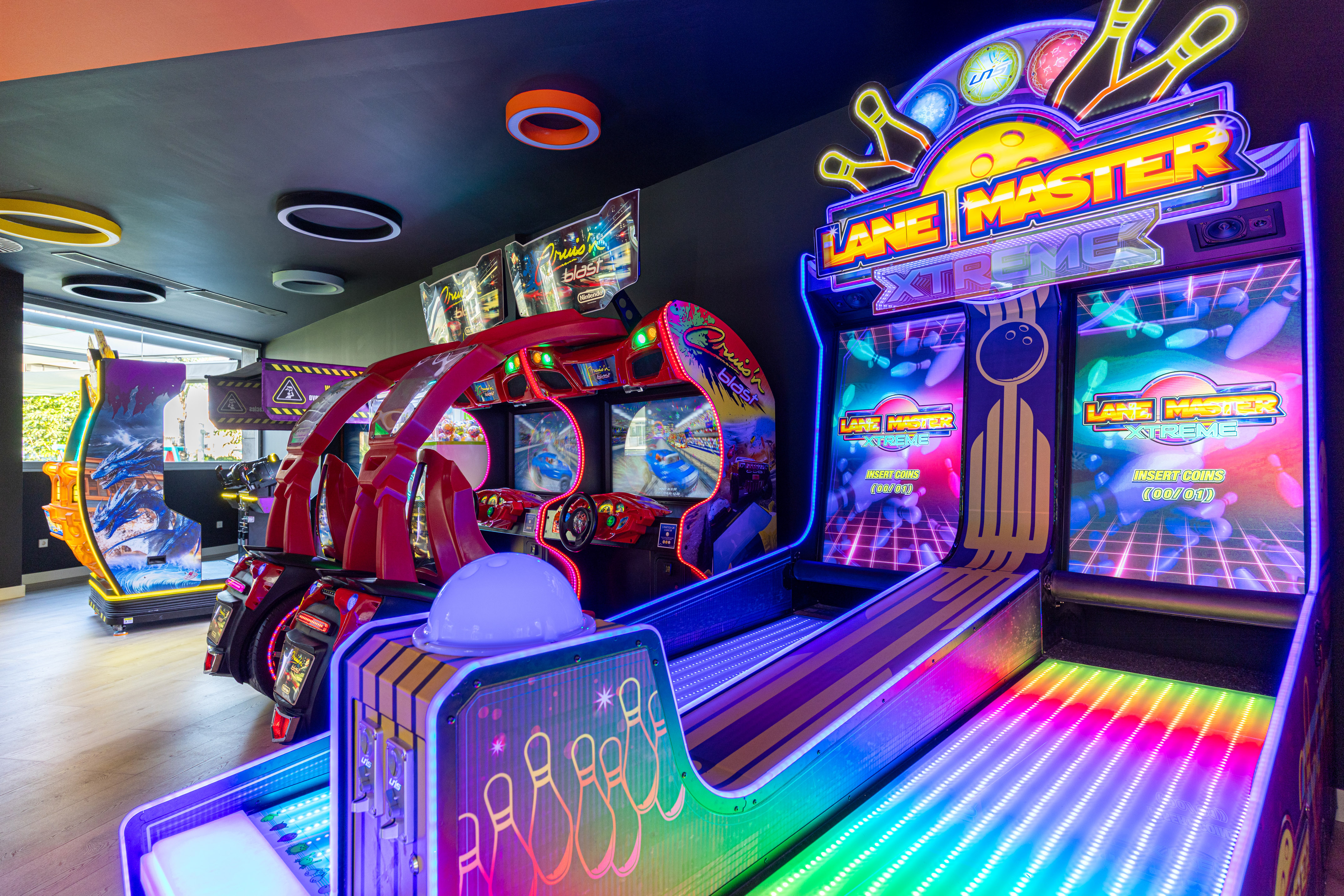 Neon-lit arcade with Lane Master Xtreme bowling and Cruis'n Blast racing games.