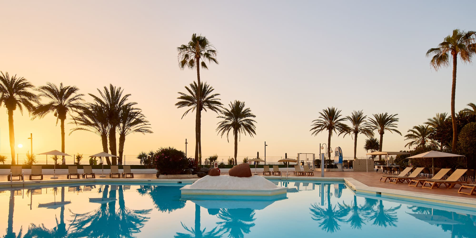 a pool with palm trees and a beach and a sunset