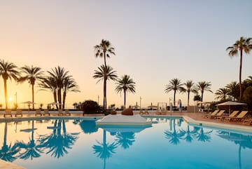 a pool with palm trees and a beach and a sunset