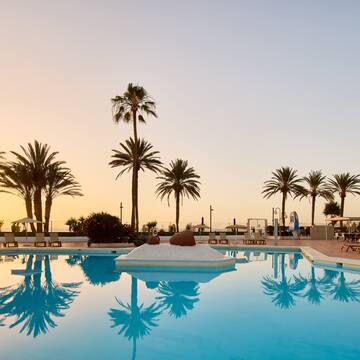 a pool with palm trees and a beach and a sunset