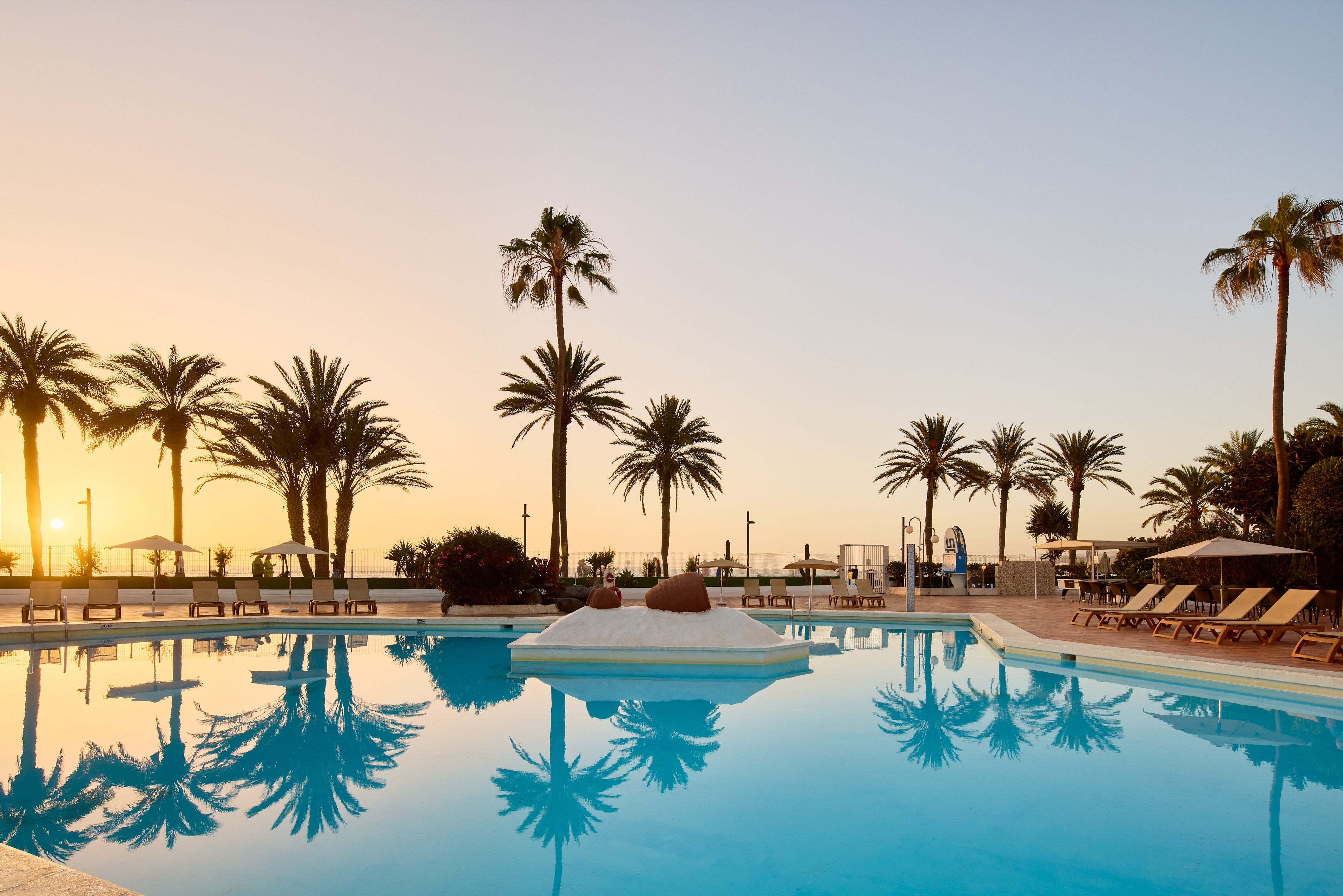 a pool with palm trees and a beach and a sunset